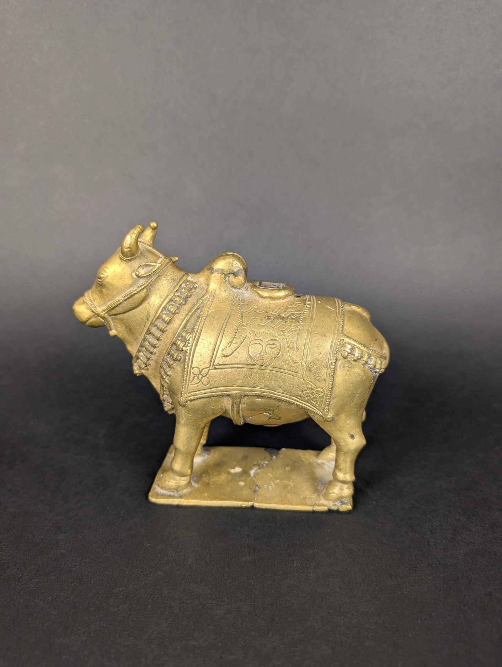 Nandi, Sacred Bull and Mount of Shiva: Nandi is richly portrayed here with a double row of bells, a blanket with an etched design of a slain lion draped over his back, and a large hump on his back. There is a part missing which would have 