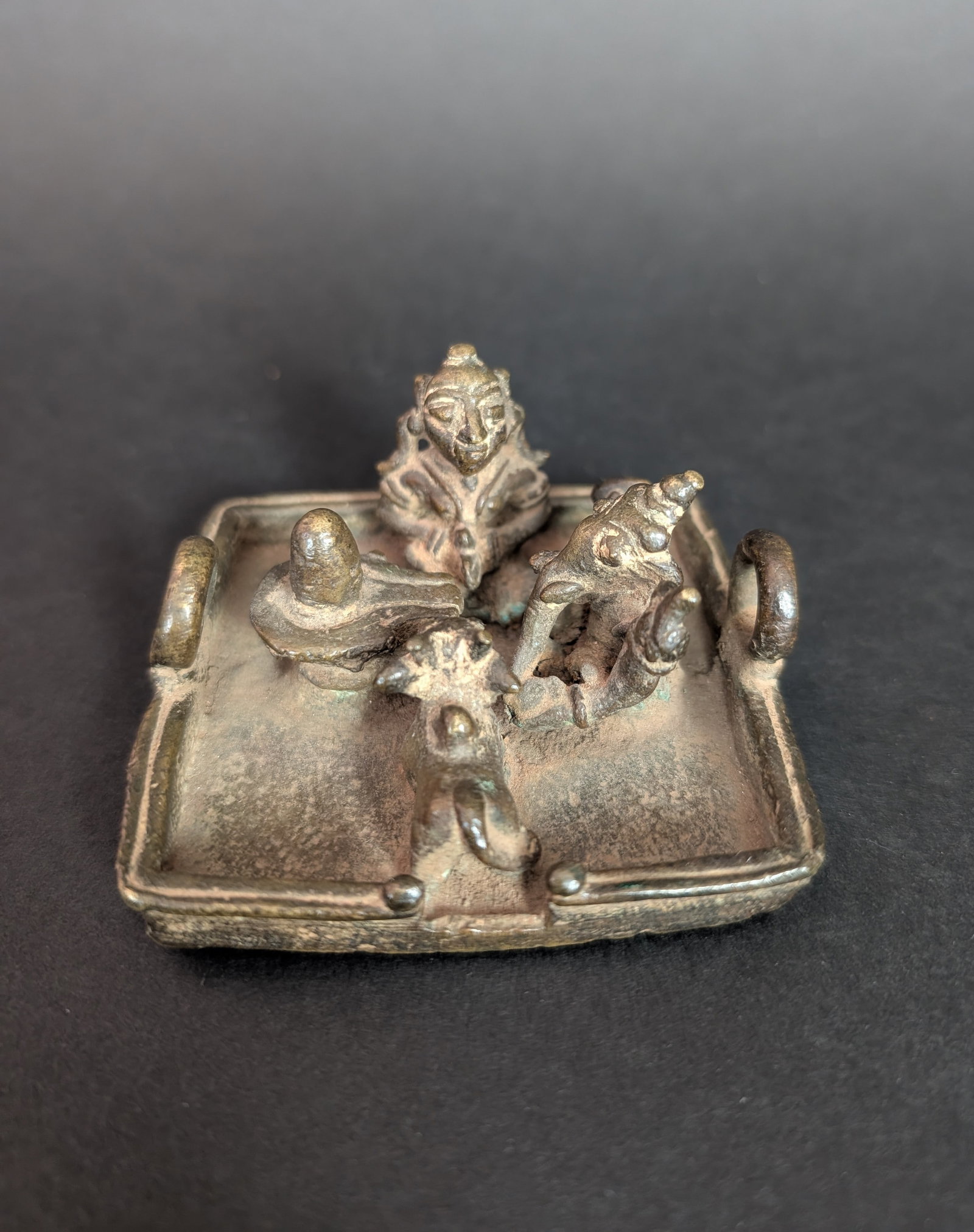 Folk Style Shiva Family Shrine: This folk bronze shows Ganesha and a female devotee worshipping a Linga, the aniconic form of Shiva. Nandi, Shiva's vahana, is a spectator. A charming bronze. Estimated age is the 19th century. Dimens