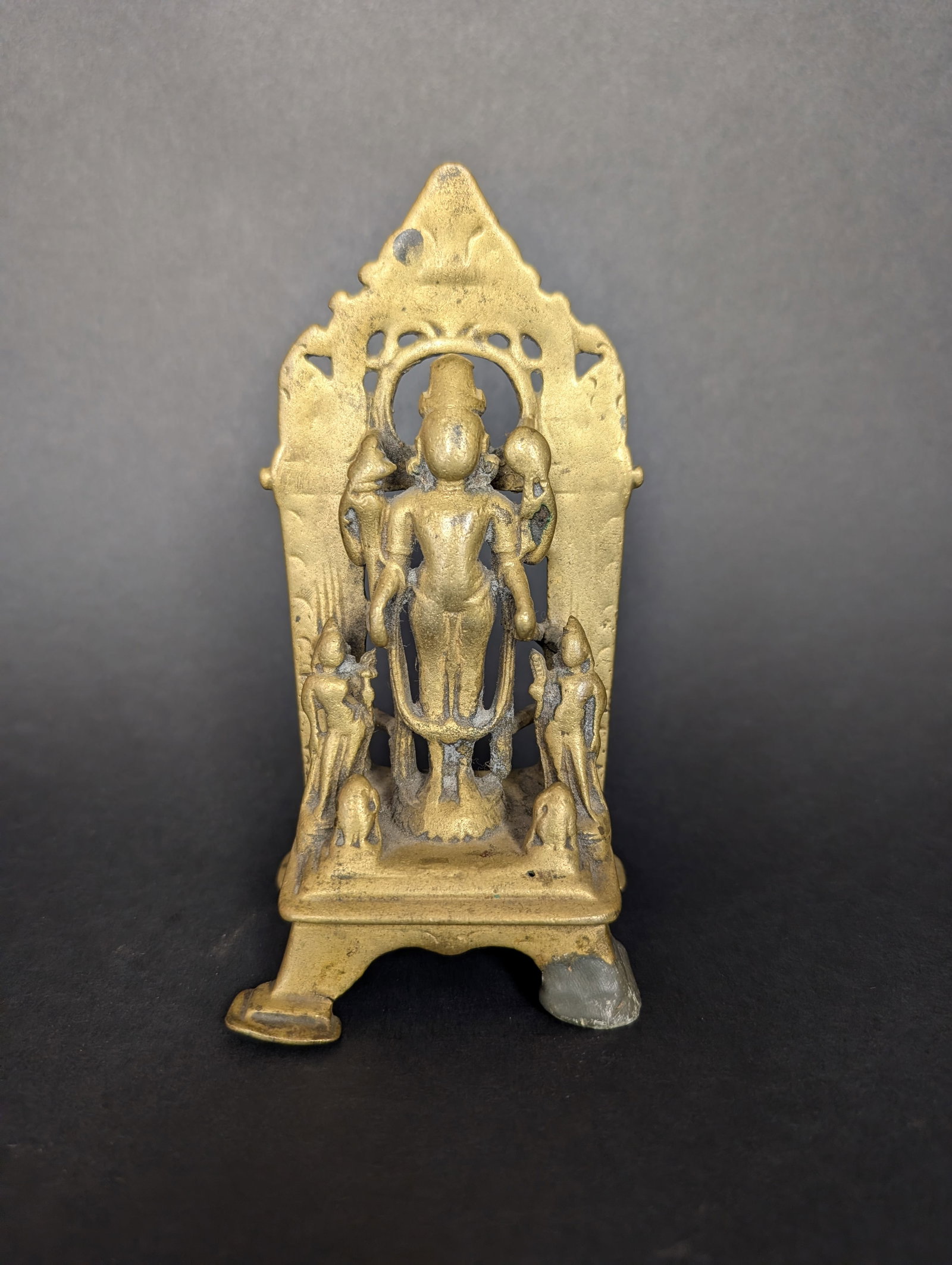 Vishnu Triad: Here Vishnu is accompanied by his consorts Sri Devi and Bhu Devi. Two attendants, possibly donors, are sitting on the pedestal. It shows centuries of ritual worship. Estimated age is the 18th century.