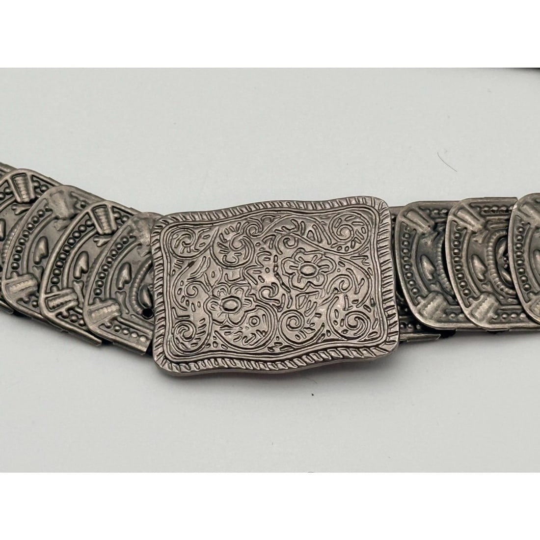 Vintage Silver-Tone Concho Link Belt: Stretch belt with overlapping embossed concho panels and floral scroll buckle; visible tarnish, rust and age-related wear