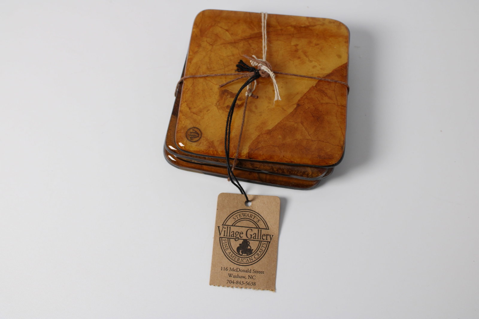Artisan Leaf Botanical Coaster Set: Set of four square coasters decorated with natural pressed leaves in amber tones. Includes original Village Gallery tag; tied together as shown