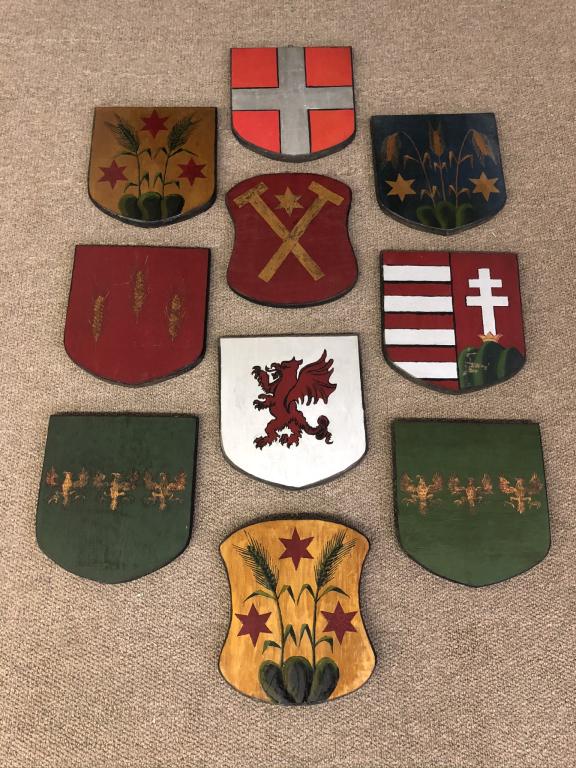 10 Armorial Shields From Camp Kwenogamac: Long Lake, NY. Each shield is hand painted with different scenes. All made out of pine and hung over the fireplace at Arpad Gerster's Camp Kwenogamac. Approximately 11 inches tall.