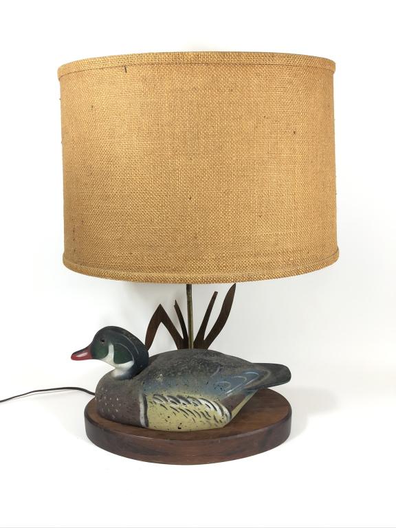 Wood Duck Table Lamp: circa 1960's. cork body duck decoy mounted on wooden base, marked on bottom The Decoy Shop, Freeport, Maine. The tip of one cattail is broken off. Burlap shade. Done in the Ken Harris Style.