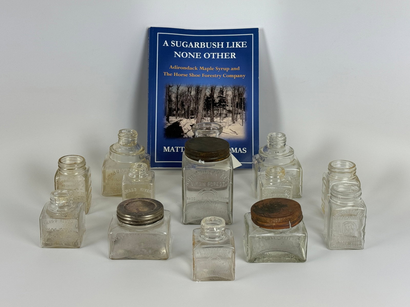 Adirondack Horseshoe Forestry Maple Syrup Jars: various sizes and style. All bottles are embossed. Includes Horseshoe Forestry sugar bush book. 12 total.