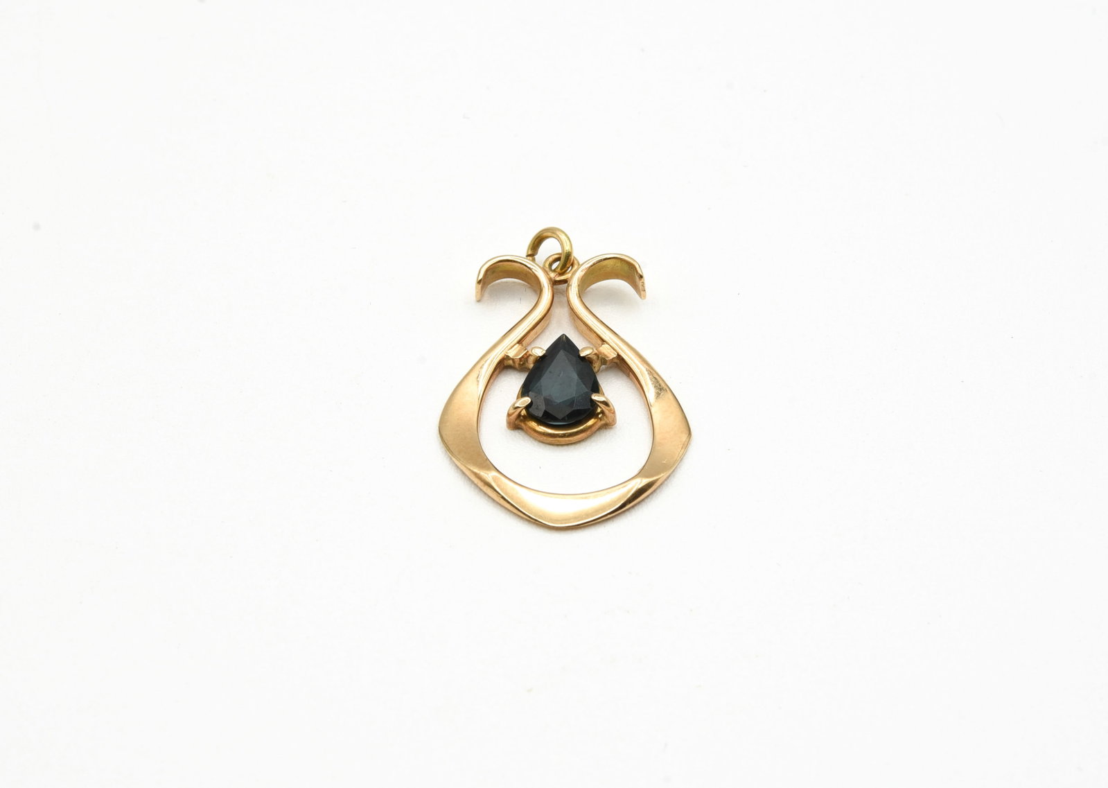14kt Gold Pendant with Sapphire: weighs 3.7grams. The 1 1/8" x 7/8" freeform pendant is an open drop shape prong-set with a pear cut dark greenish blue color zoned sapphire of fair to good quality. 6.4 x 8.9 mm and 2.5mm deep.