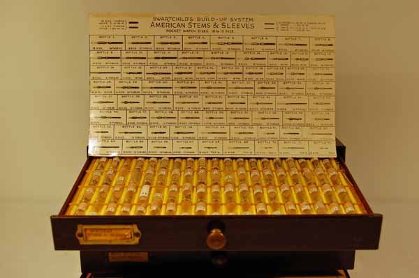 American Pocket Watch Co. New Old Stock: in a watchmakers mahogany grained metal 2 part 4 drawer cabinet. 12" x 6" x 7". Provenance: from an estate in Middlebury, VT along with a collection of clock, watchmakers and jewelers tools; numerous 