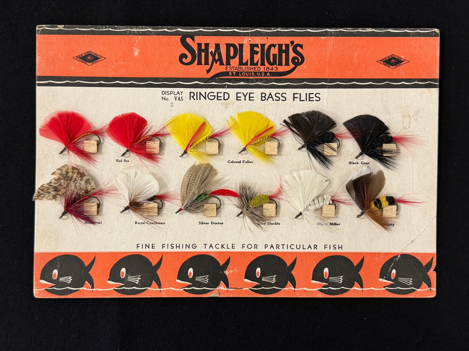 Shapleigh's Bass Fly Store Card: Rare 11 7/8" x 8" store display card retaining all 12 Ringed Eye Bass Flies still hooked to the cork mounts, each with a printed pattern identification. The card has light wear/bends, a few tack holes