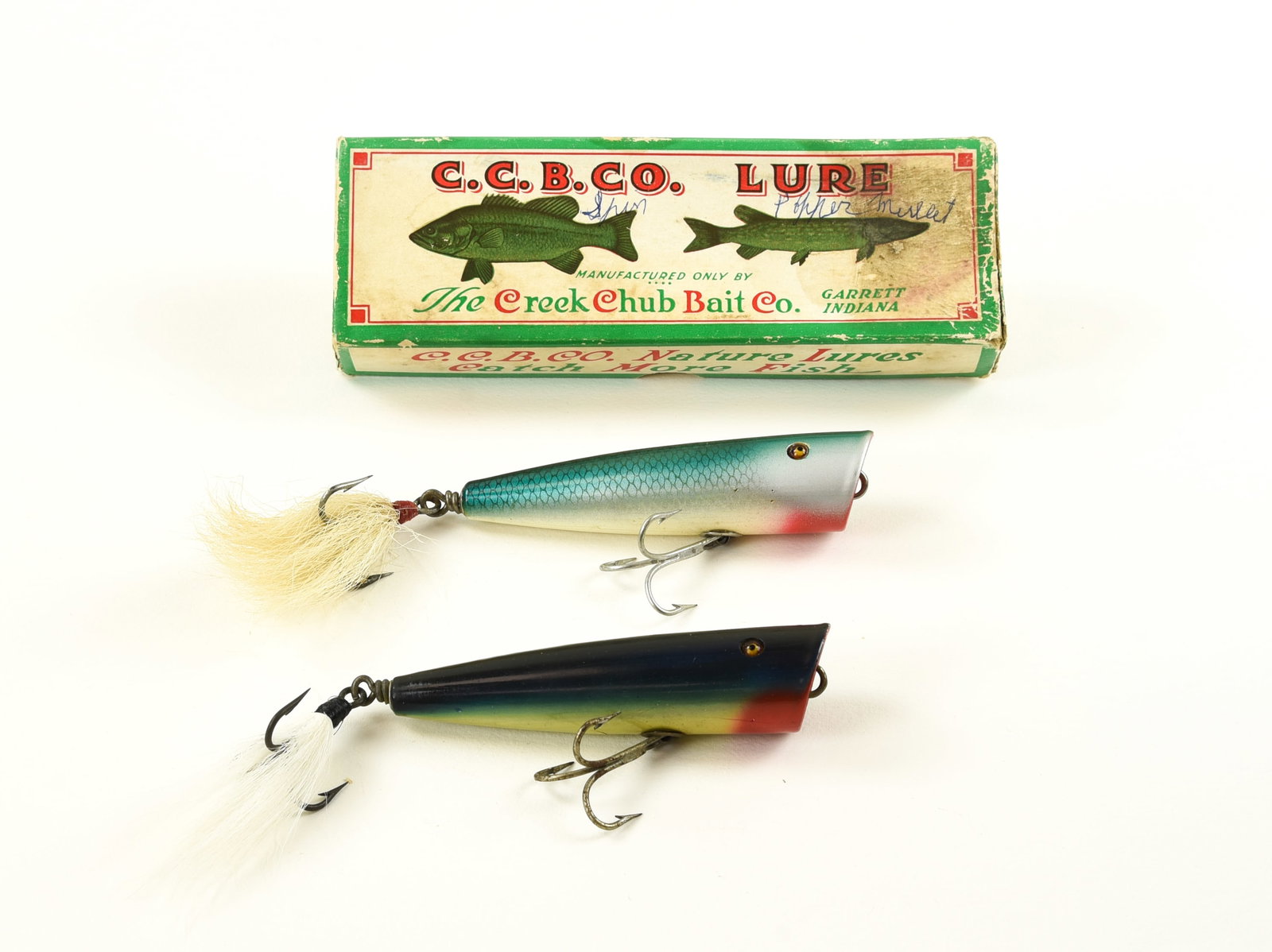 2 Creek Chub Snook Plunkers: Includes a bright blue mullet Snook Plunker with bucktail, shiny Ex- with light wear/soiling, a few small pointers and tight age lines, coming in the correctly stamped 7107 BT box, rough but solid. An