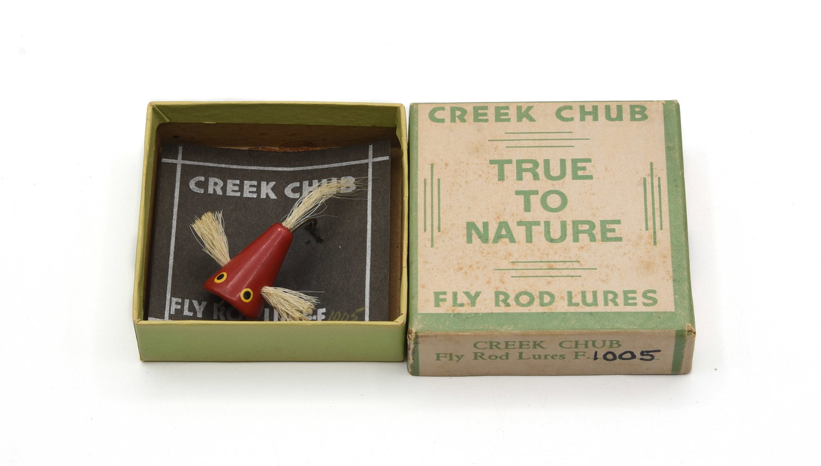 Creek Chub Flyrod Plunker Bass Bug: Red finish with white hair wings and tail, about Ex condition with light wear/soiling a lip edge nick. Coming in a True To Nature box with later handwritten 1005 on one flap, hooked to an old black ca