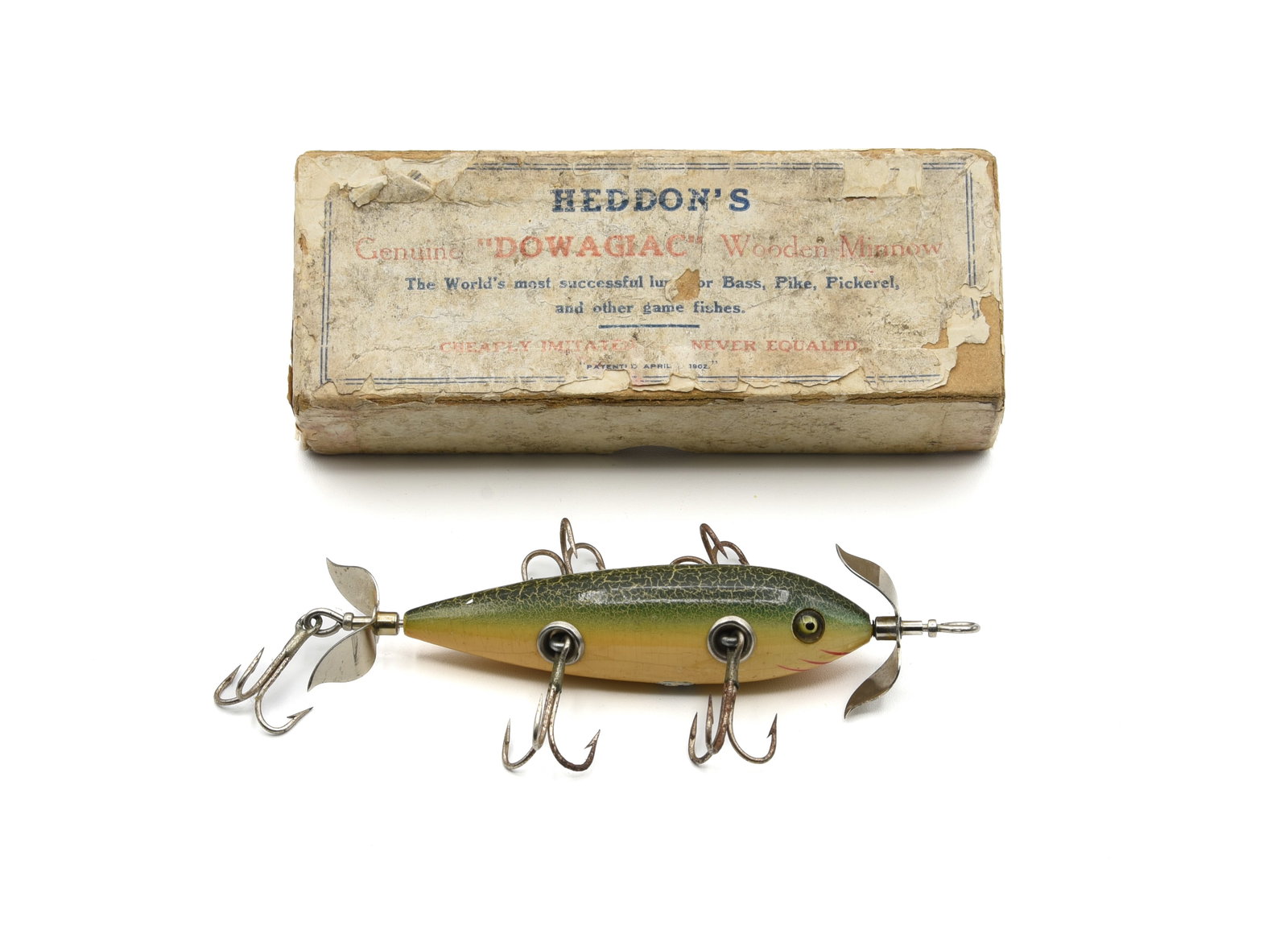 Heddon's "Dowagiac" Wooden Minnow Box: Pre-1910 white pasteboard box, rough but solid with most text is legible, some paper loss and unstamped for model/color. Housing an early 5hk minnow finished in green crackleback with hand painted gil
