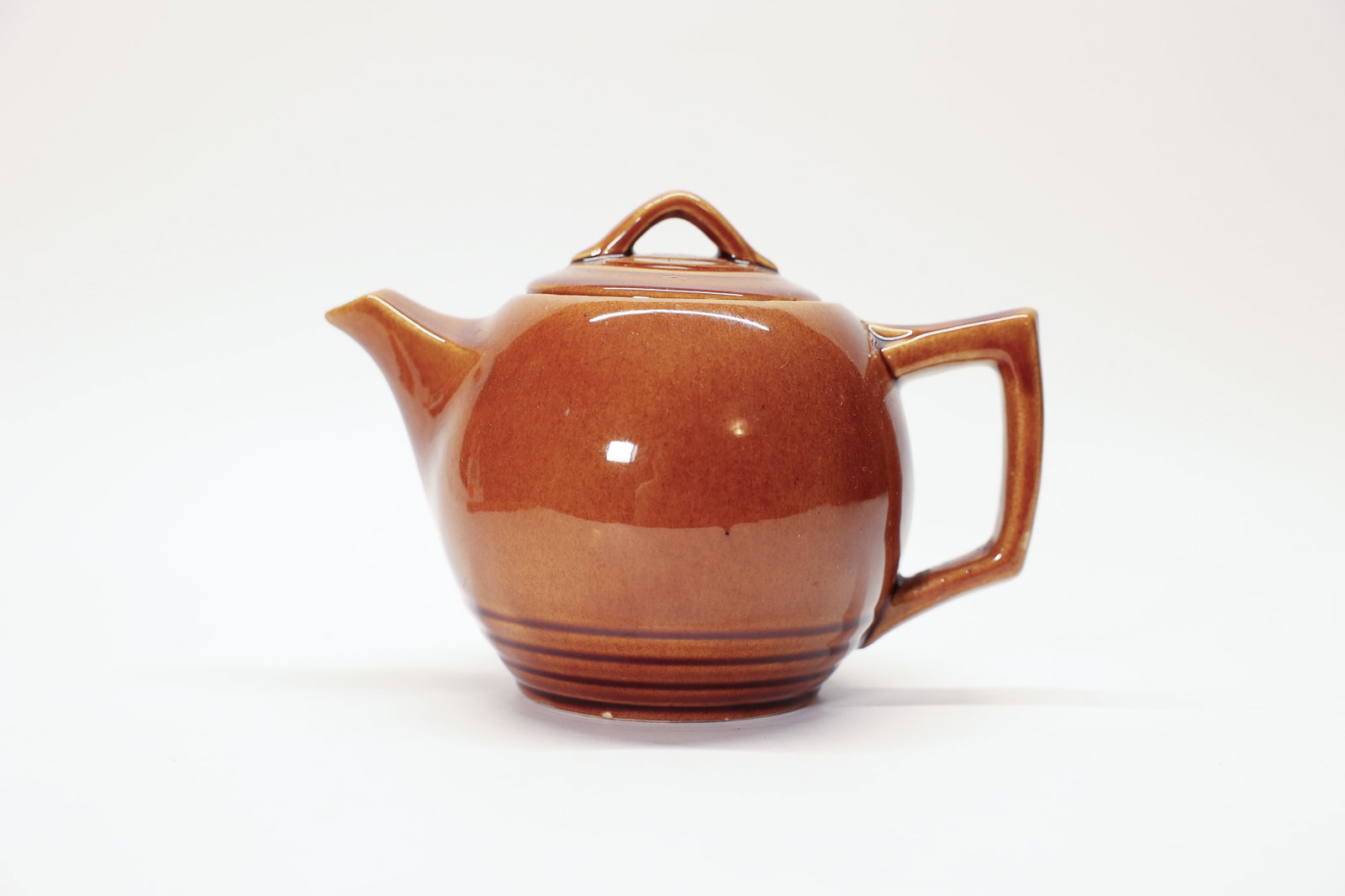 Vintage McCoy Pottery Brown Teapot USA: Vintage McCoy Pottery teapot in a warm caramel-brown glaze, featuring a bulbous rounded body with subtle horizontal ribbed banding near the base and a soft two-tone shading effect. The teapot has a sc