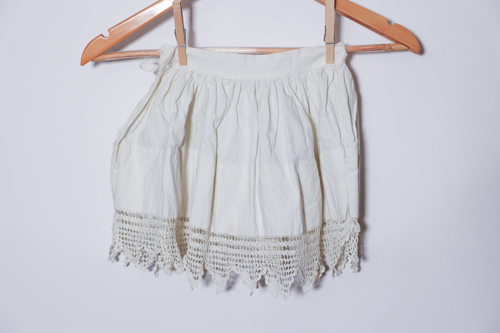 Antique Child's Cotton Petticoat Crochet Lace: Charming antique child's white cotton petticoat featuring a gathered waistband and a deep, hand-crocheted lace hem finished in a pointed scalloped pattern. The lightweight cotton body shows natural pe