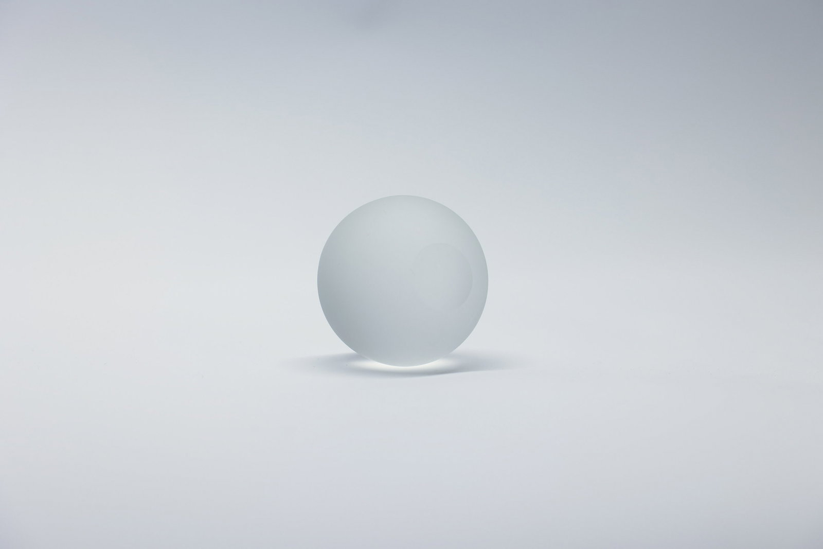 Frosted Glass Sphere Paperweight 2x2": A minimalist frosted glass paperweight in a clean spherical form, measuring 2 x 2 inches. The soft, matte frosted finish gives the glass a gentle, diffused glow, with subtle internal shading that
