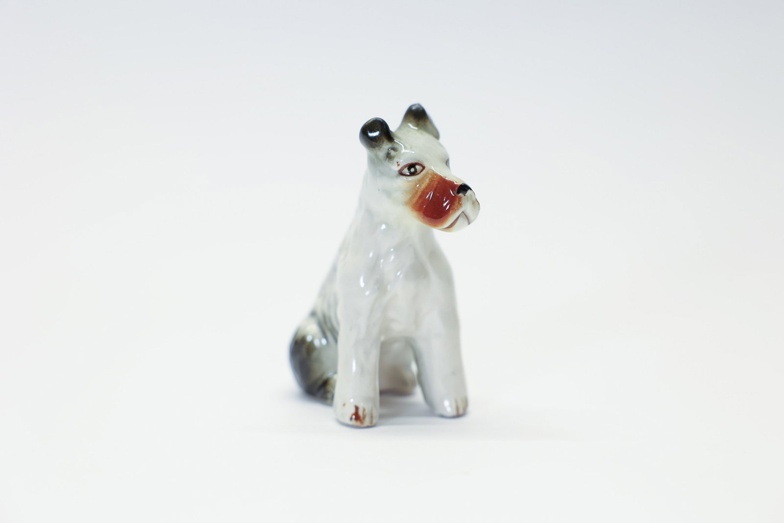 Vintage Fox Terrier Porcelain Figurine 3.5": Description:A sweet vintage porcelain figurine of a seated fox terrier, 3 1/2 inches tall, captured in an alert seated pose with perky ears and an attentive expression. The glossy glaze features