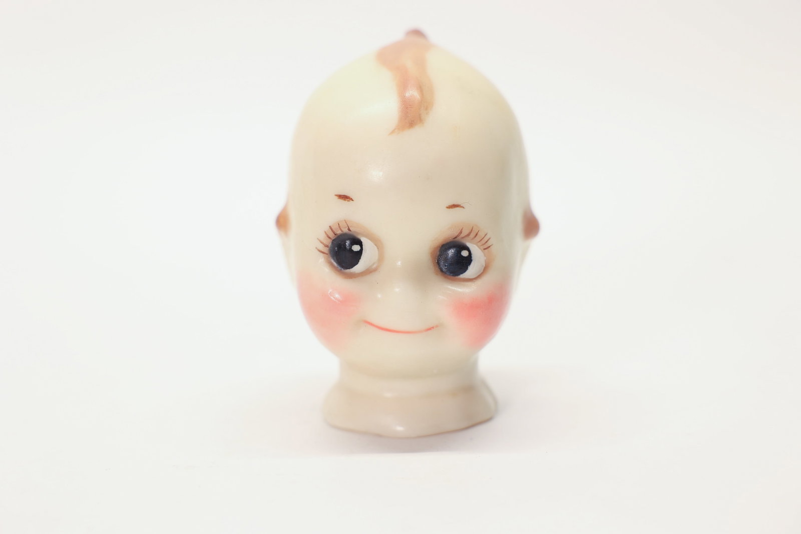 Antique Kewpie-Style Wax Doll Head: 4.5" tallA sweet antique wax doll head, sculpted in the beloved Kewpie style with the character's signature side-glancing painted eyes, rosy cheeks, tiny topknot curl, and gentle smile. The soft wax m