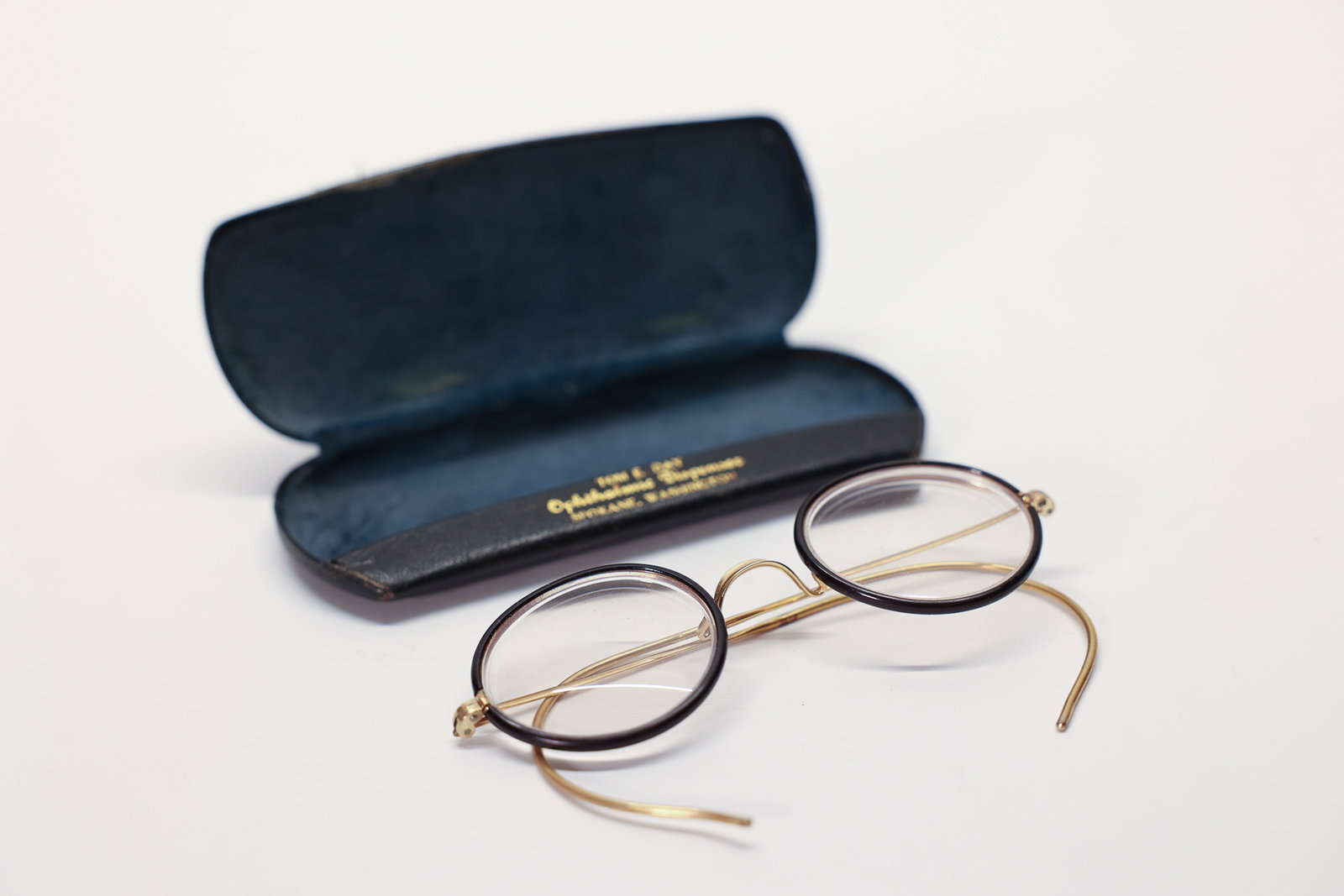 Antique Round Gold Eyeglasses w/ Tom Day Case: A charming pair of antique round eyeglasses featuring gold-tone wire frames with tortoise/dark rim accents, paired with their original hard case stamped in gold lettering "Tom E. Day, Ophthalmic Dispe