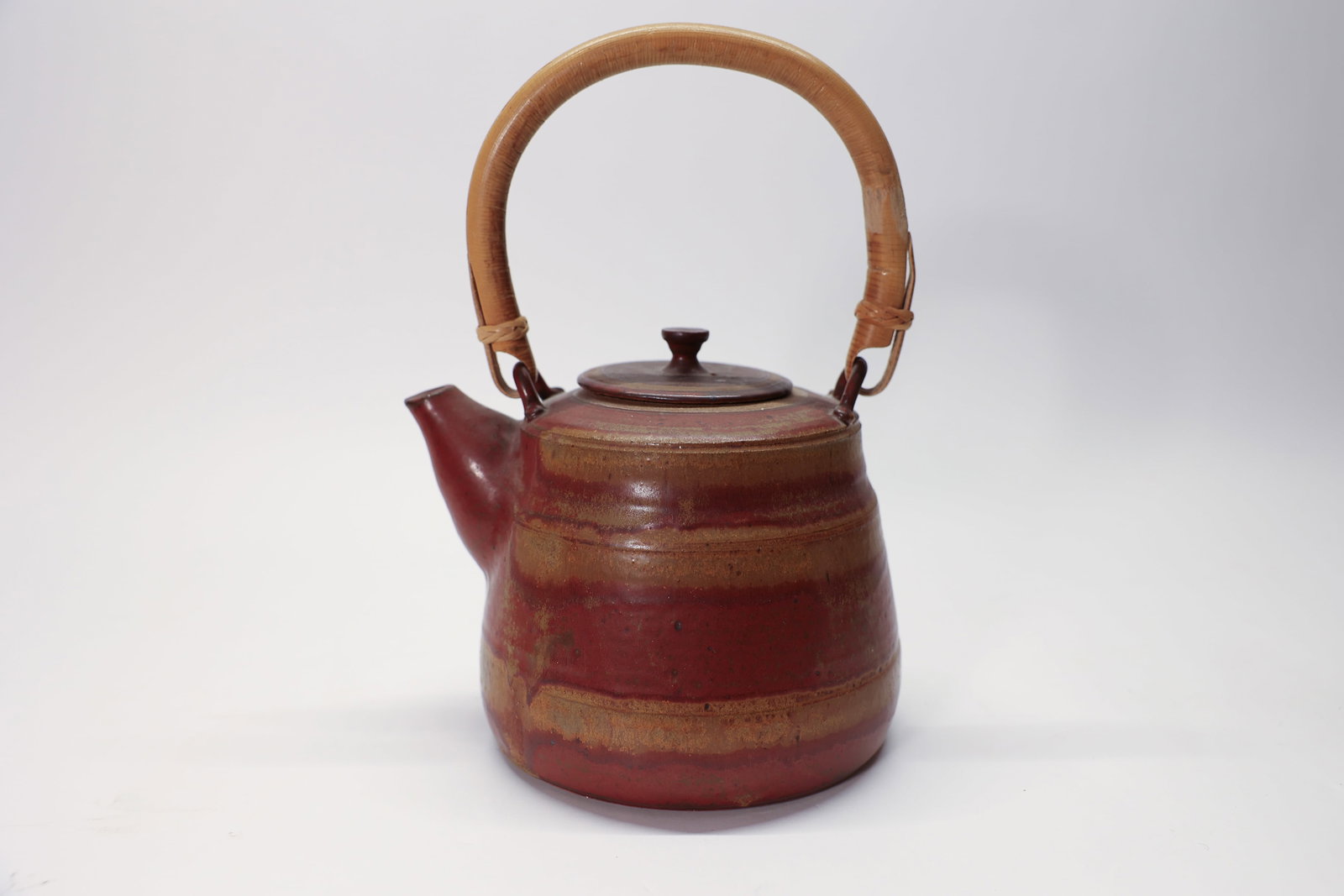 Studio Pottery Teapot Signed Bamboo Handle: 11 1/4" tall x 6" dia. A beautiful handmade studio pottery teapot featuring a striking multi-toned glaze in deep oxblood red and warm speckled tan, applied in horizontal banded striations for a rich,
