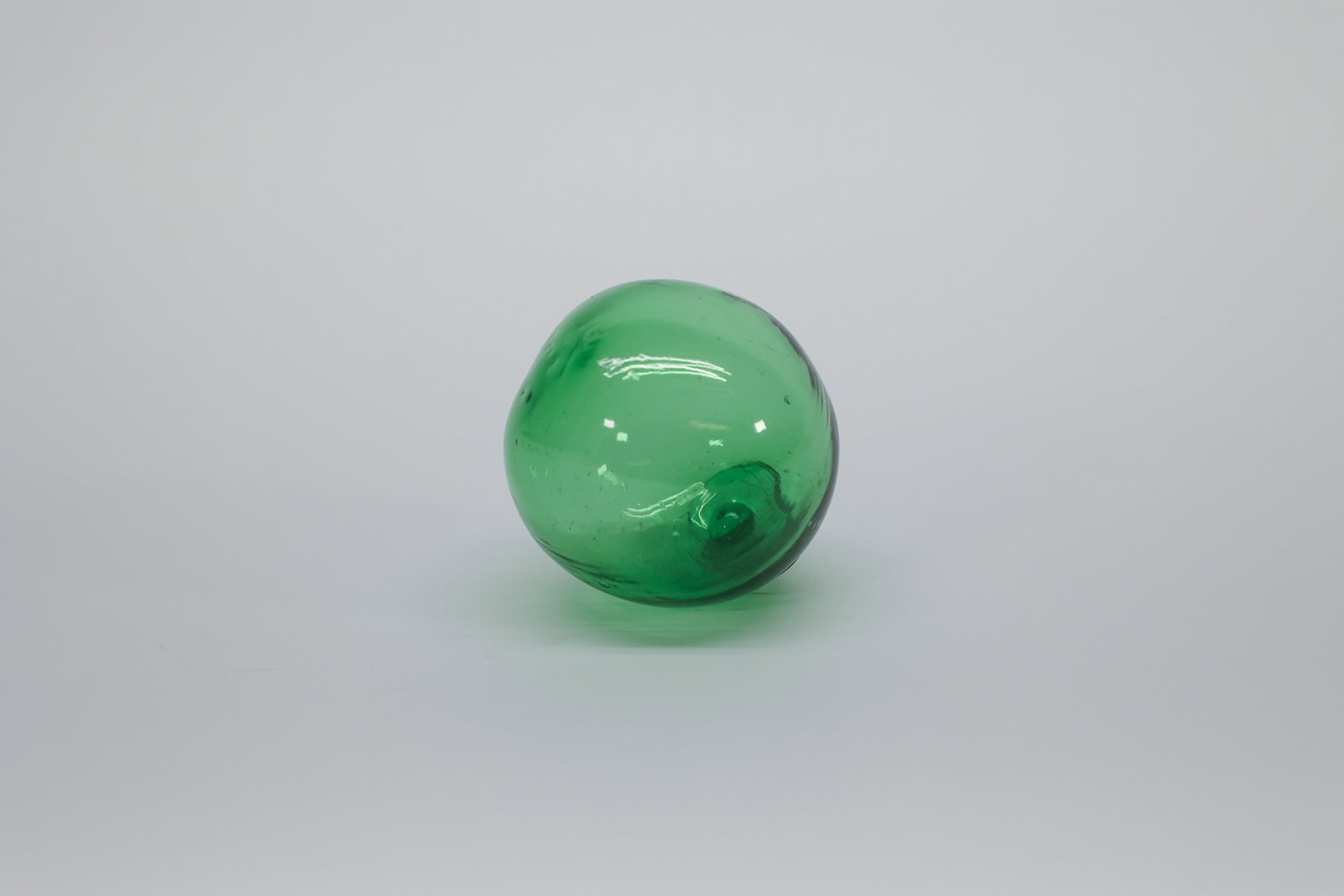 Green Hand-Blown Glass Fishing Float, 3": Hand-blown green glass fishing float, 3" diameter. Visible pontil mark and applied sealing button at the pour end, with embedded air bubbles and swirl striations characteristic of hand-blown