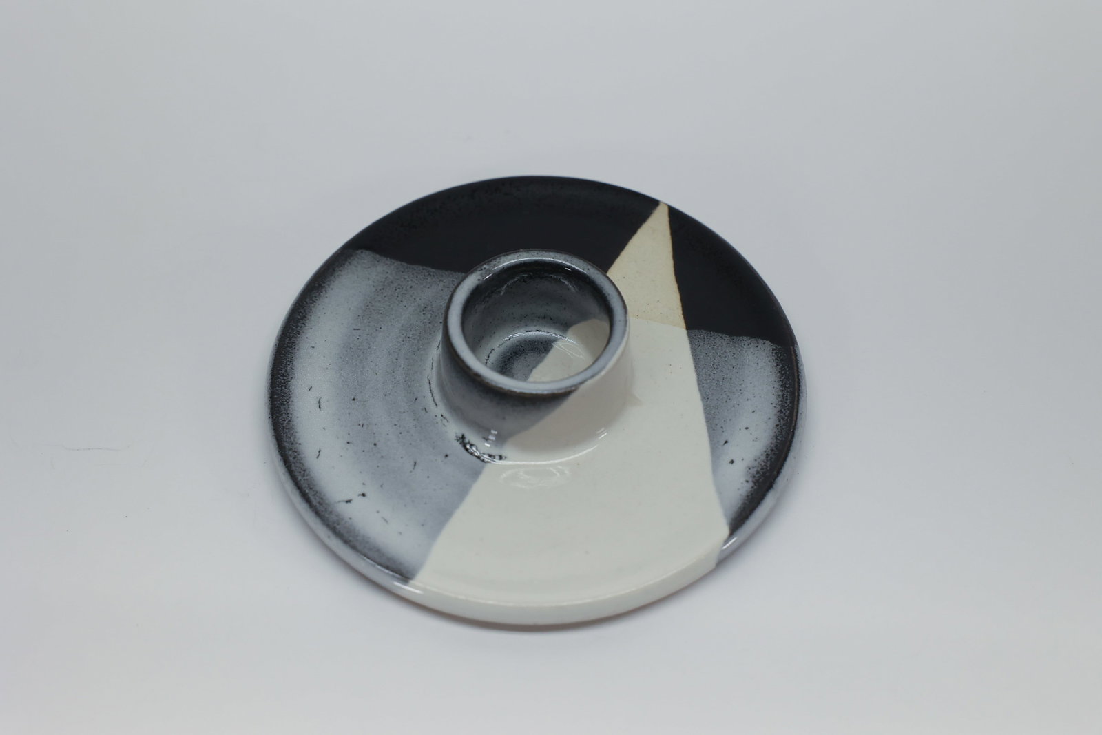 Studio Pottery Color-Block Candle Holder Dish: Handmade studio pottery candle holder with wide dish base and raised center socket. Color-blocked glaze in black, gray, and cream geometric wedges. Impressed maker's mark on the underside.Dimensions: