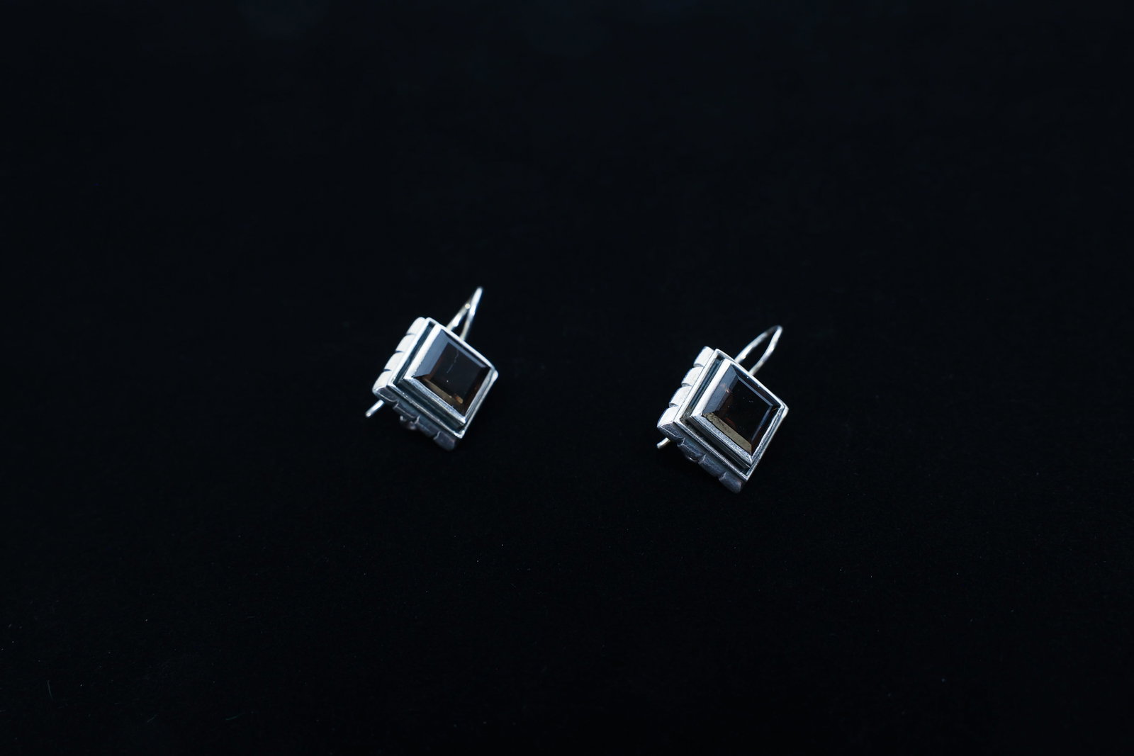 Sterling Silver Smoky Quartz Drop Earrings: Pair of sterling silver square drop earrings, each set with a bezel-set square-cut smoky quartz stone framed by a ribbed silver border, on shepherd's hook wires.Marked 925Dimensions: W: 0.5", L: 1"