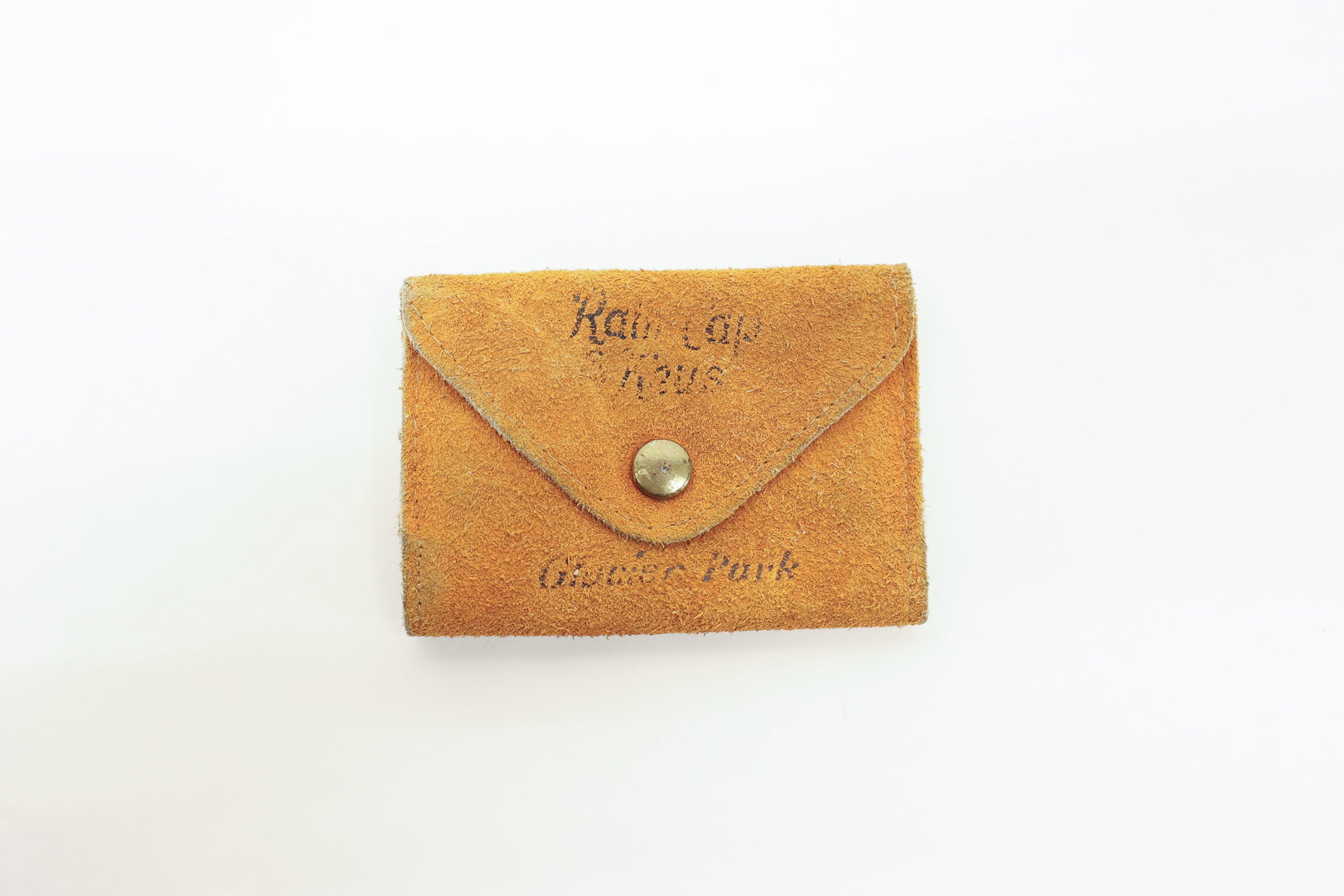 "Rain Cap Keys" key holder Glacier National Park: Suede leather snap-close key case advertising "Rain Cap Keys" and "Glacier Park," with a fold-out six-hook key rack inside secured by a brass snap.Dimensions: H: 0.5", W: 2.5", L: 3.5"