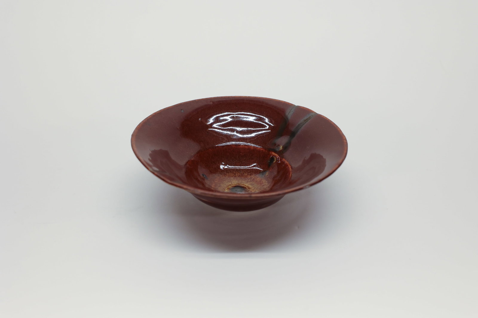 Studio Pottery Bowl, Brown Glaze: Wide, shallow studio pottery bowl in a deep brown glaze with dark iron-oxide streaking and a golden-brown crackled well at the center, flared rim, unglazed foot ring. Incised signature on the