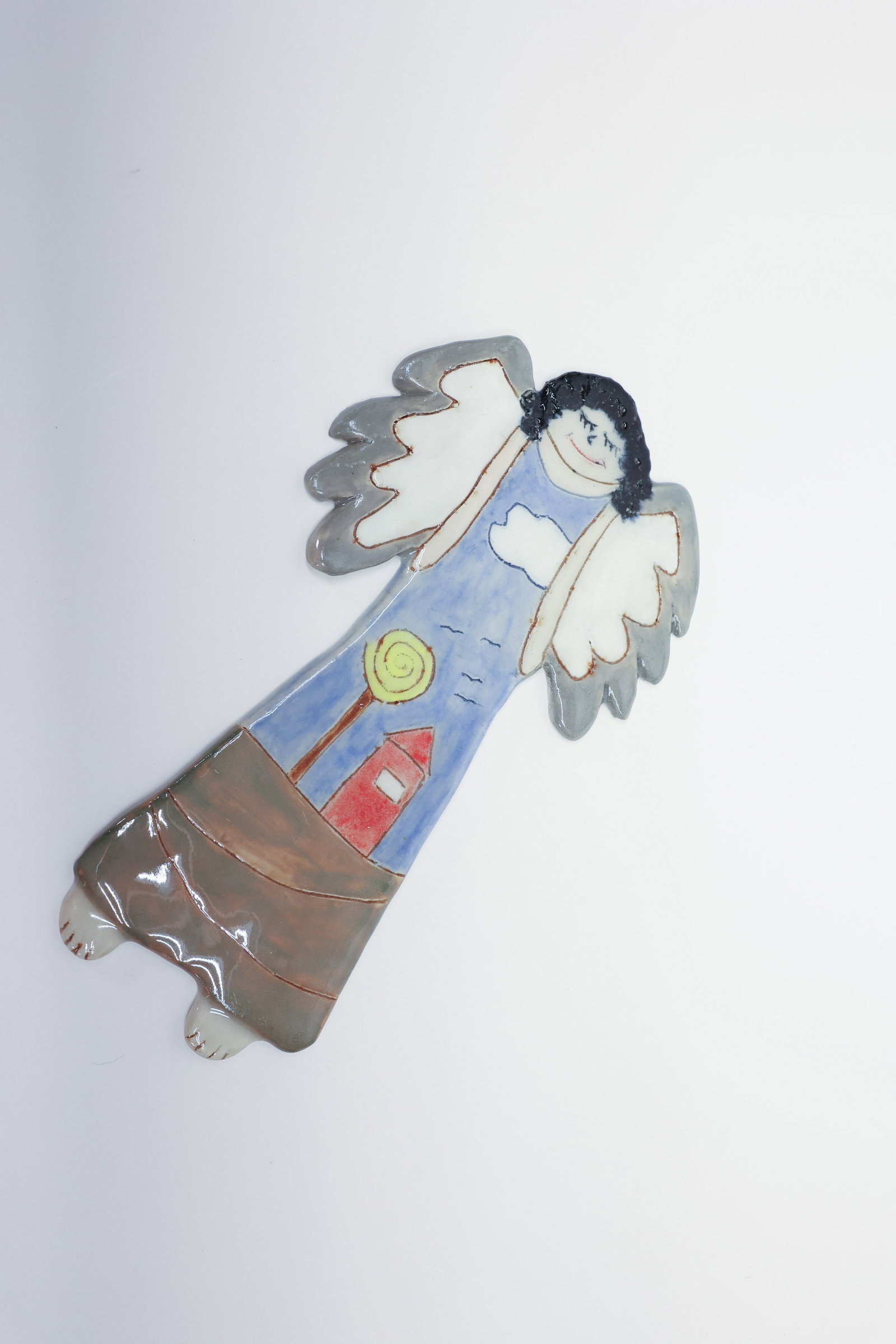 Folk Art Ceramic Angel Wall Plaque, Signed 2024: Handmade ceramic angel plaque in a whimsical folk art style, hand-painted with a smiling face, dark curly hair, layered dove-gray wings, and a robe decorated with a red-roofed house, a sun, and