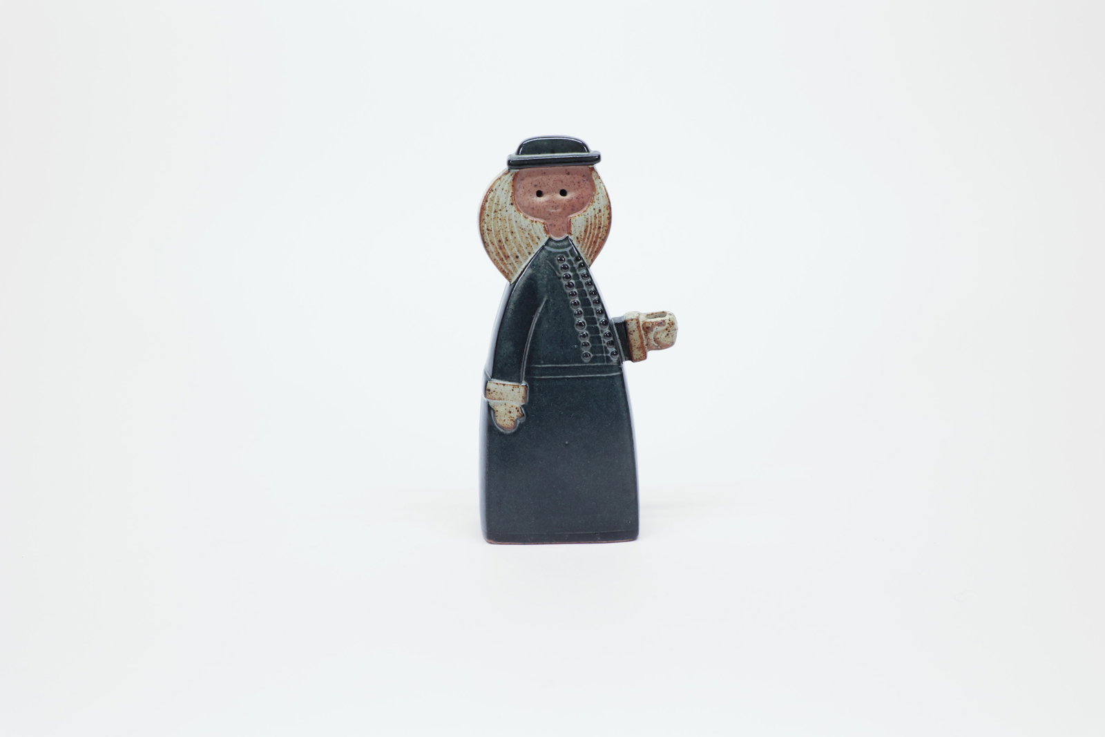 Mid-Century Japanese Stoneware Candle Holder: Mid-century stoneware figural candle holder, likely Japanese-made, depicting a bonneted figure in a dark green robe with a row of button detailing down the front, holding a small cup-form candle socke