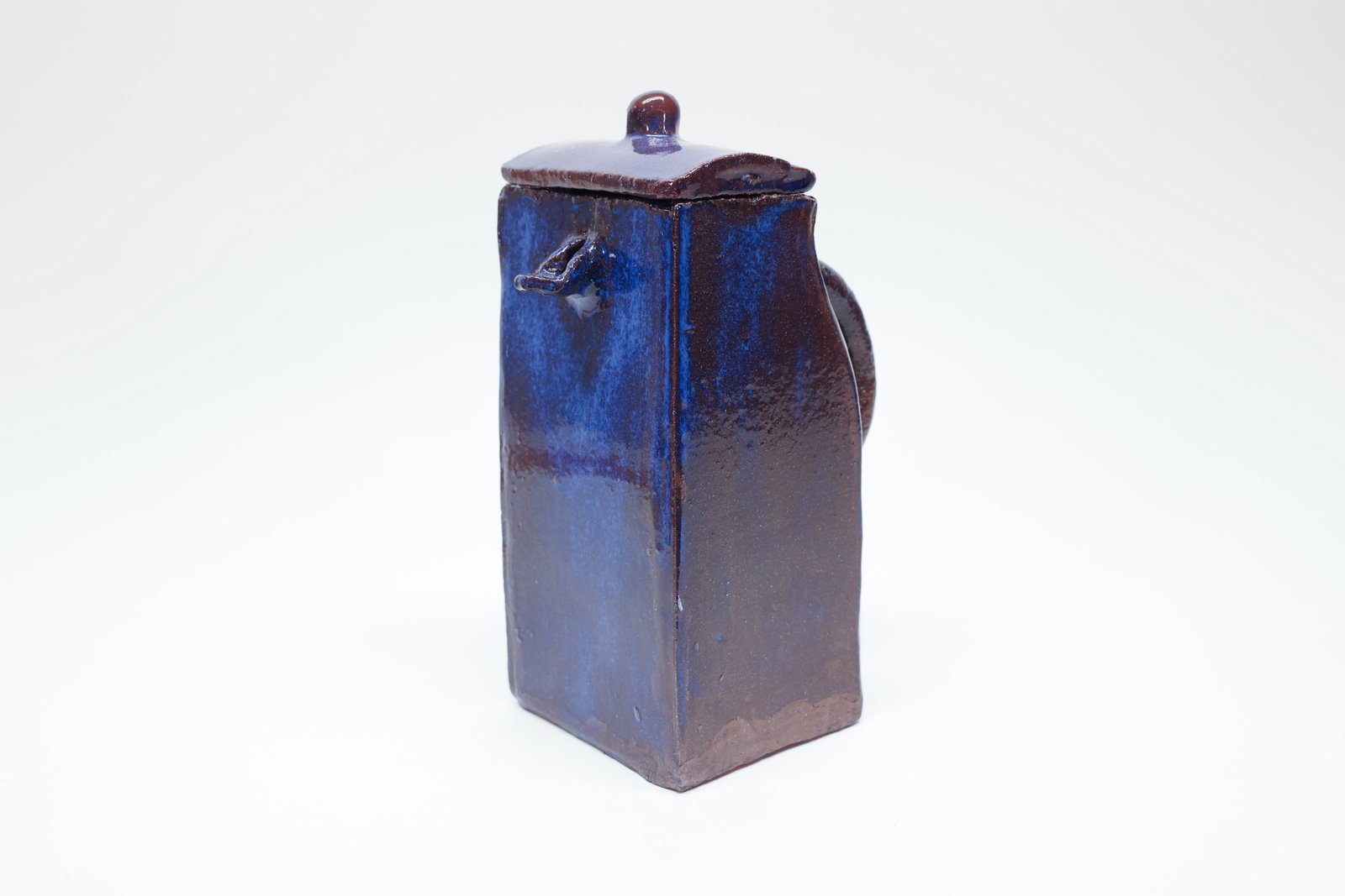 Edward Lee Folk Art Pottery Lidded Jug: Signed folk art style pottery lidded jug by Edward Lee, hand-built in a tall rectangular form with rounded corners, finished in a rich cobalt-blue running glaze over a warm terracotta clay body that s