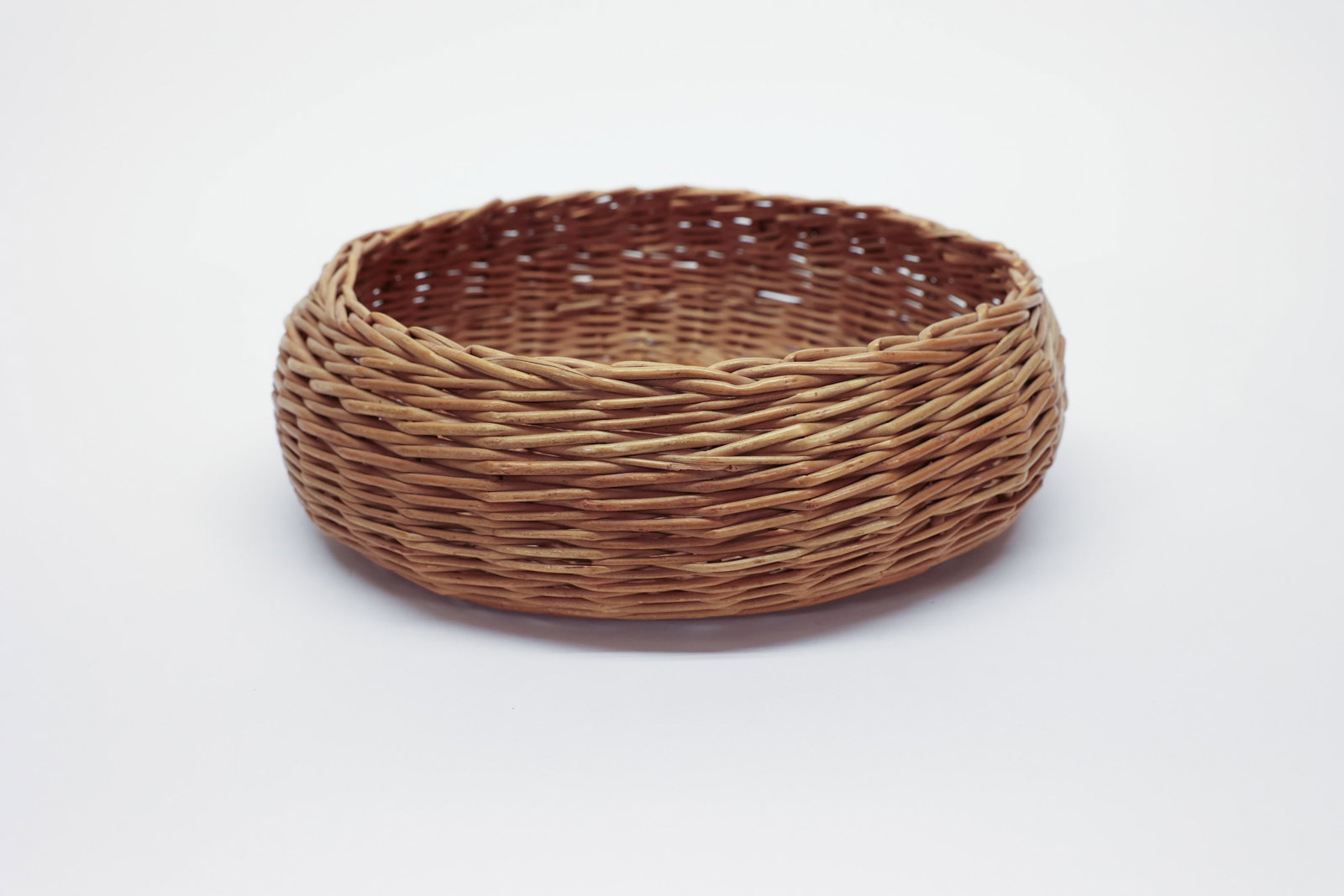 Woven Wicker Basket, Low Round Bowl: Low, round wicker basket, hand-woven from willow or rattan reed in a tight radial pattern that spirals out from a small square center base. The shallow bowl form and natural honey-brown tone make it a