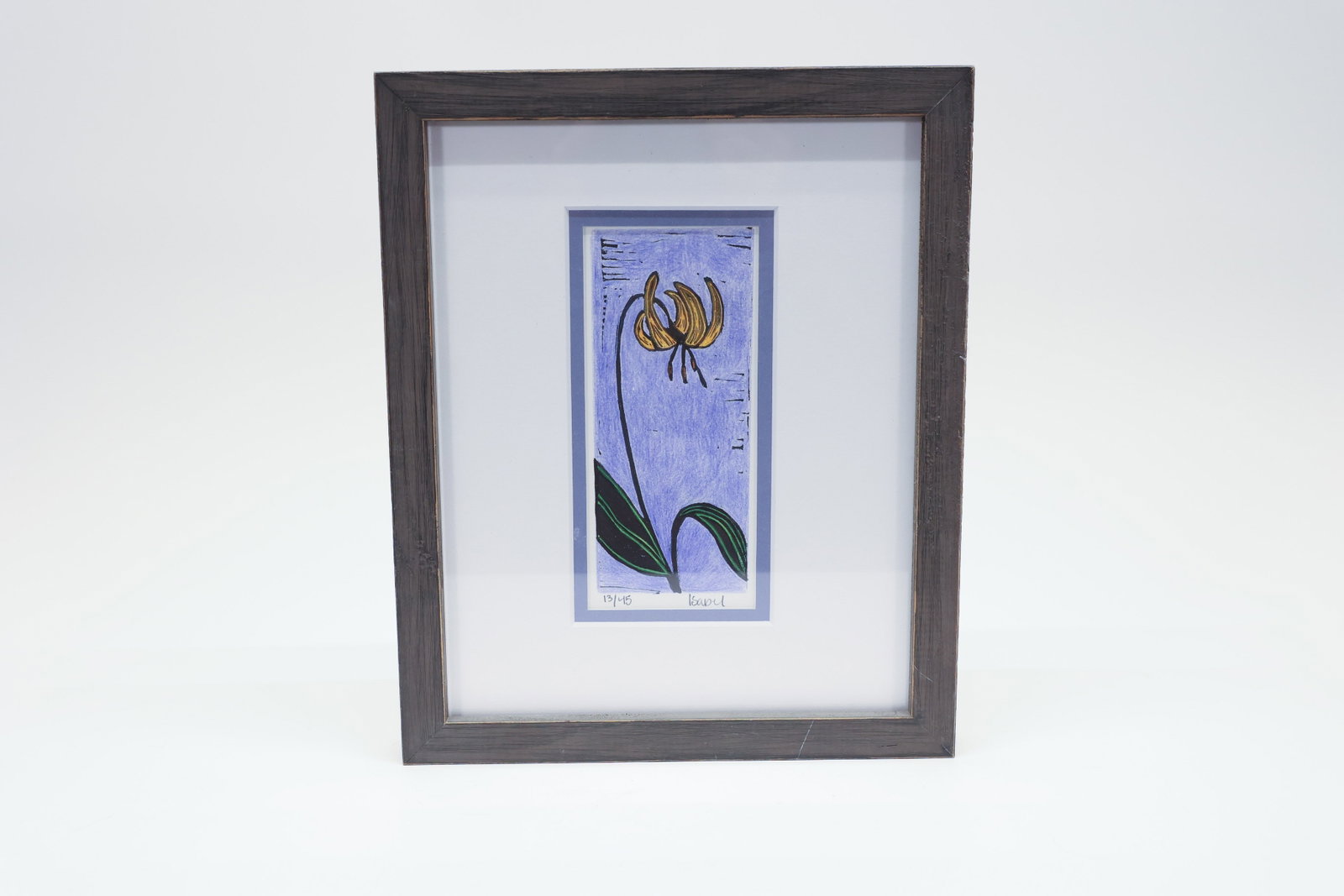 Signed Glacier Lily Block Print, Framed: Hand-colored block print depicting a glacier lily in nodding bloom, its recurved gold petals rendered in bold black linework against a hand-tinted lavender-blue ground. Glacier lily is a native wildfl