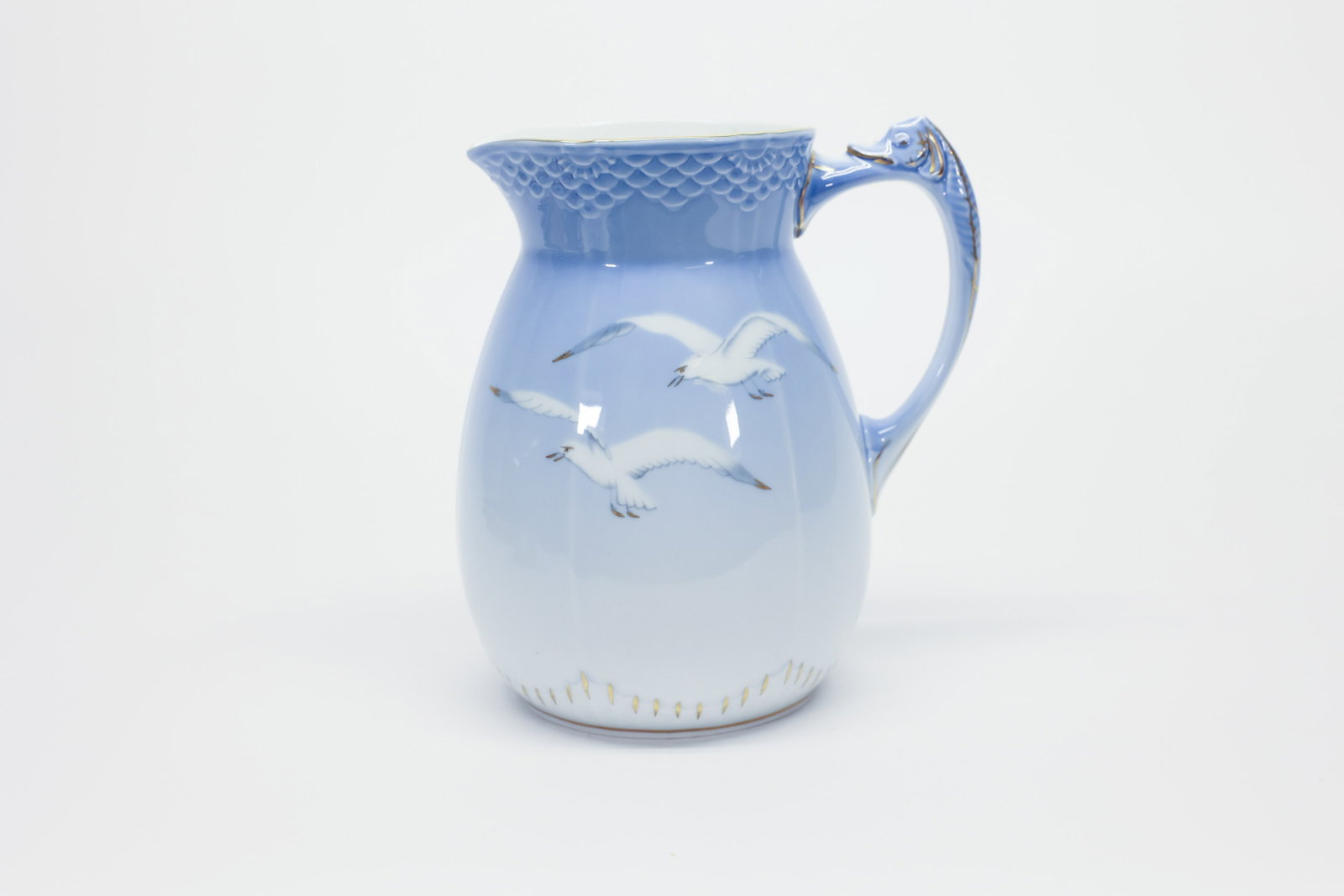 Bing & Grøndahl Seagull Pitcher, Denmark #84: Bing & Grøndahl porcelain pitcher in the classic Seagull (Måge) pattern, featuring soft blue-gray gulls in flight against a graduated blue-to-white ground, gilt trim, and a scalloped,