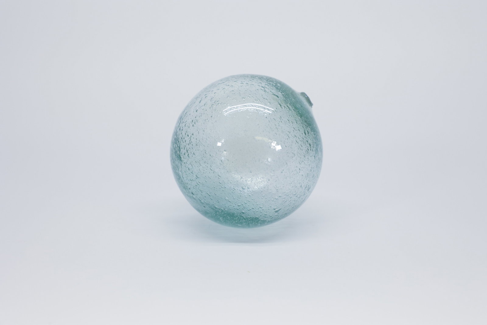 Aqua Glass Fishing Float: Hand-blown glass fishing float in pale aqua glass, spherical form with a pontil scar and visible seed bubbles throughout the glass, characteristic of early hand-blown floats. Unmarked.Dimensions: W: 4