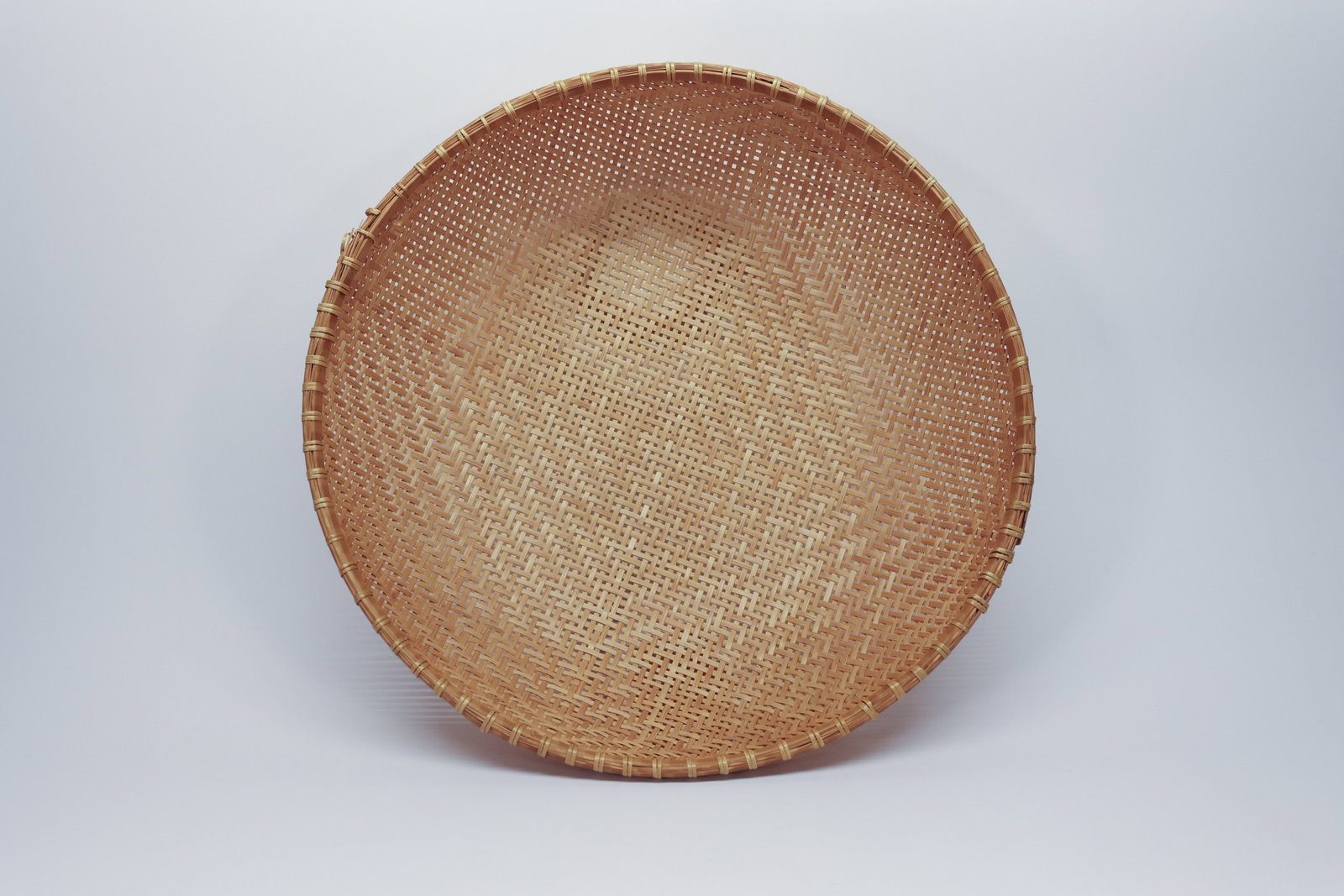 Large Woven Bamboo Winnowing Basket, 17": Large hand-woven bamboo winnowing basket, featuring a tight diagonal twill weave that fans out from the deep center to a wide, gently curved rim reinforced with wrapped bamboo binding. Traditionally u