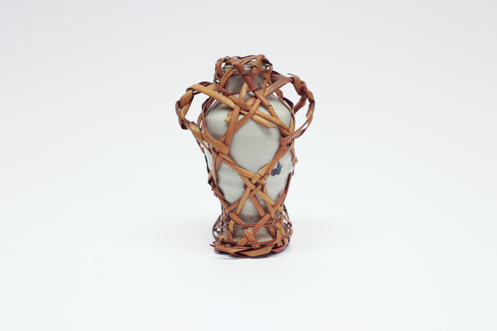 Vintage Japanese Bamboo-Wrapped Pottery Vase: This small stoneware vase is encased in a loosely woven lattice of split bamboo or rattan, gathered into a pair of loop "handles" at the shoulder — a decorative wrapping technique long associated wi