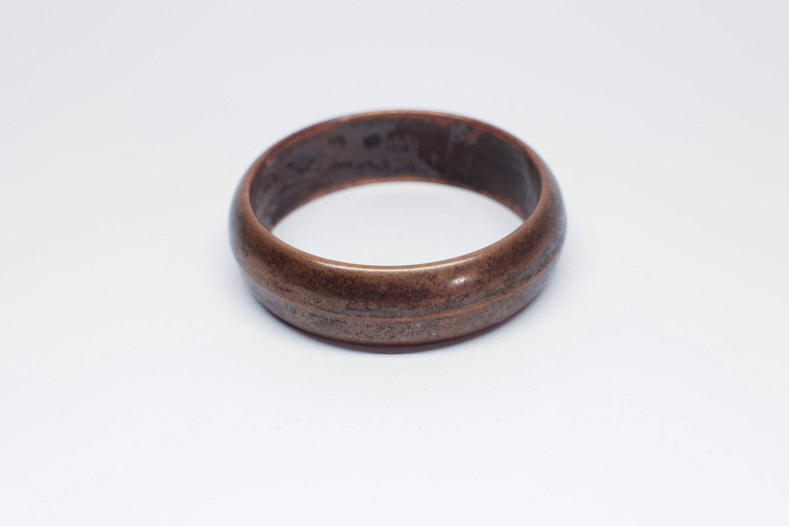 Wide Hollow Copper Tone Bangle Bracelet: A wide, hollow-form bangle bracelet in a warm copper/bronze tone, with a smooth rounded outer profile and a 2.75" inside diameter. The metal has developed a mottled, mixed patina of darker oxidation
