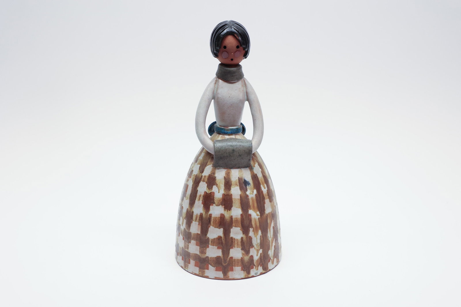 Jordi Aguade Spanish Folk Art Figurine: This 10" ceramic figurine depicts a woman in a full, flared bell-shaped skirt, hollow-cast with an open base typical of ceramic figure construction. She's rendered in a charming folk-art style, with a