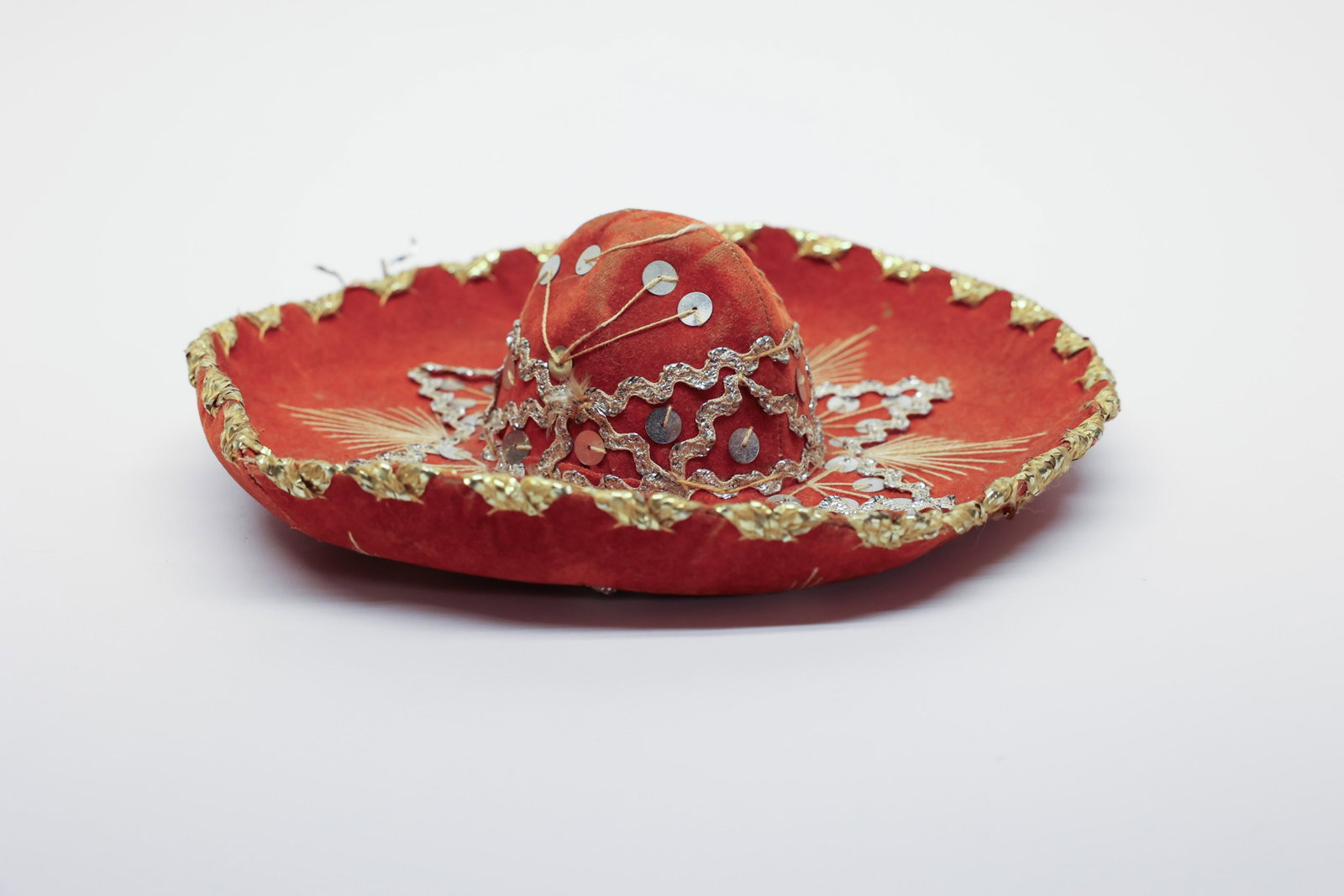 1960s Miniature Mexican Sombrero: Description:A festive miniature souvenir sombrero, 9" wide, made of orange velvet trimmed all around the brim in gold metallic scalloped braid. The crown and brim are hand-embroidered with radiating