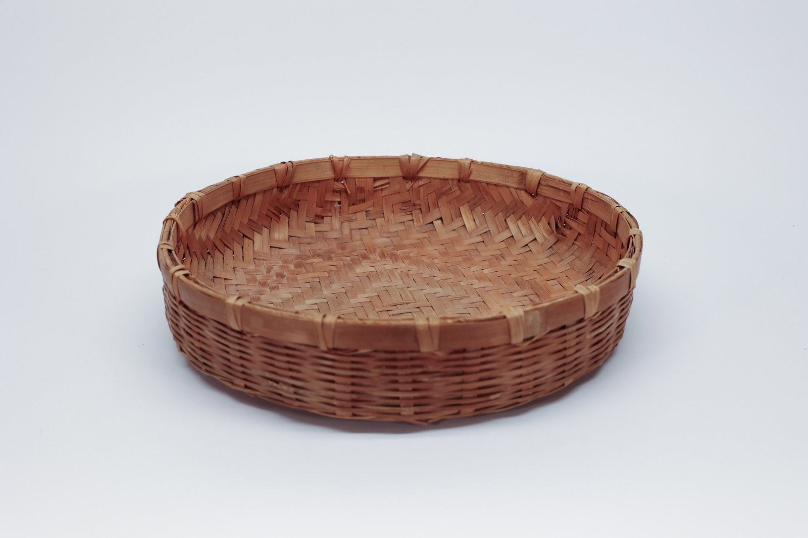 Woven Bamboo Winnowing Tray, 12 3/4": A well-made woven bamboo tray, 12 3/4" in diameter, with a herringbone diagonal weave across the interior floor and a sturdy wrapped rim reinforced with split bamboo binding at intervals. The undersid