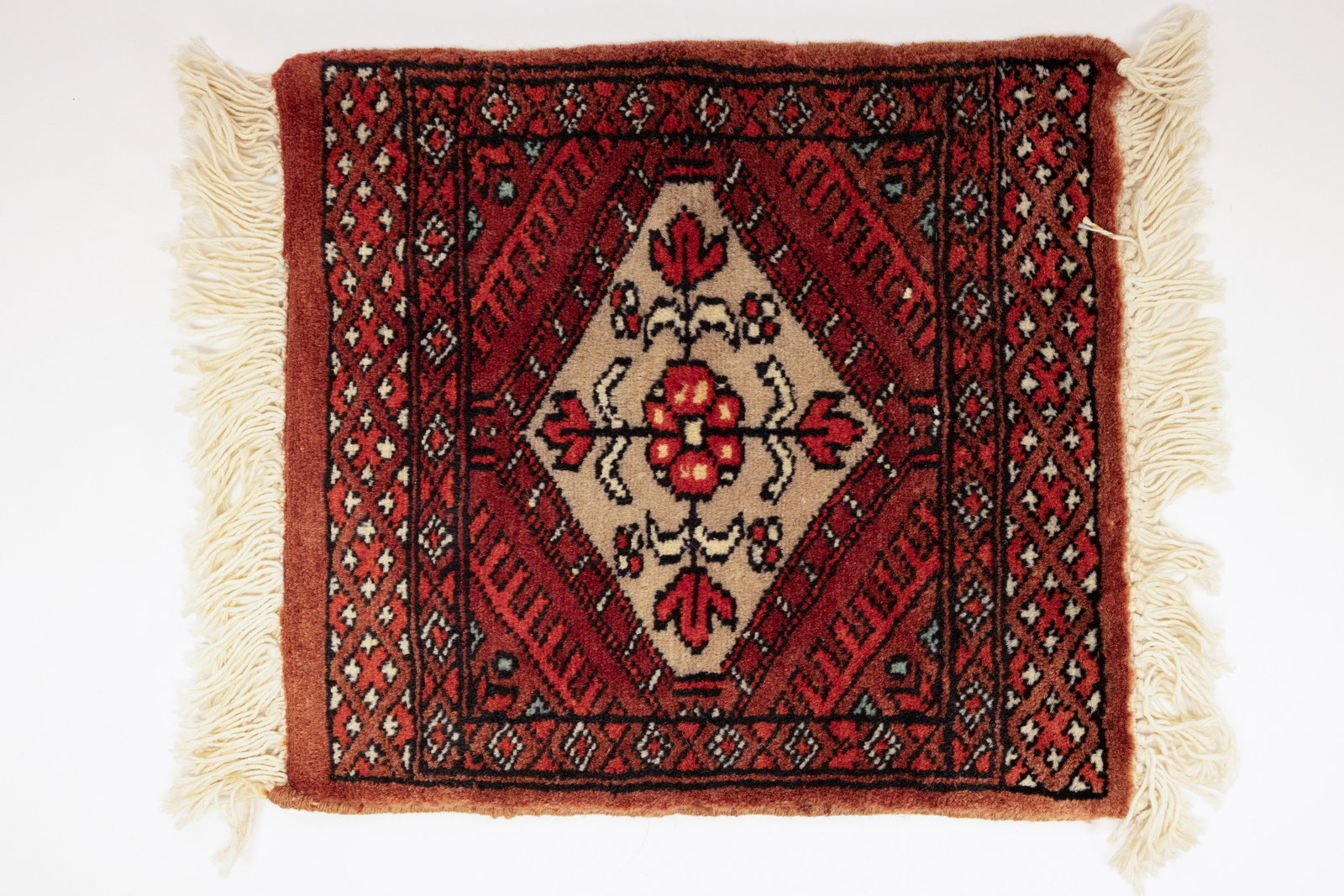 Small Hand-Knotted Baluch Tribal Wool Rug: Description:Small hand-knotted wool tribal rug/mat with a central diamond medallion on an ivory ground, filled with a stylized floral motif and flanked by geometric and diamond border designs in rust
