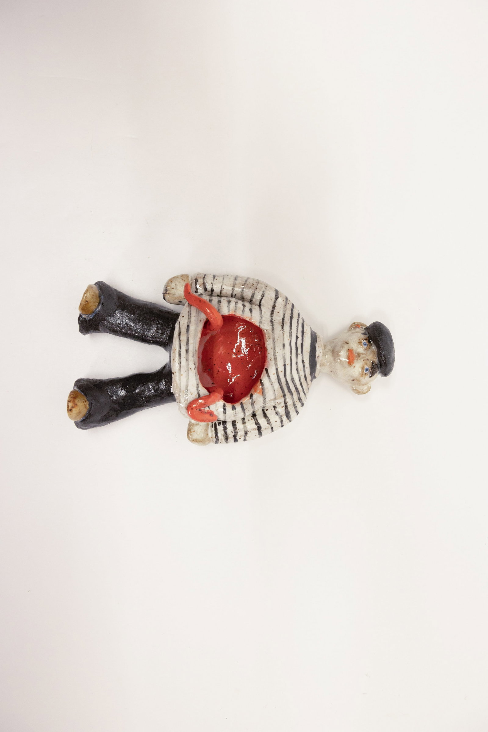 Surreal Art Pottery Sailor Figure, Disemboweled: Description:Hand-built flat-backed ceramic figure of a sailor or fisherman, wearing a black beret and a striped Breton-style shirt over black trousers, depicted with a graphic, surreal wound at the