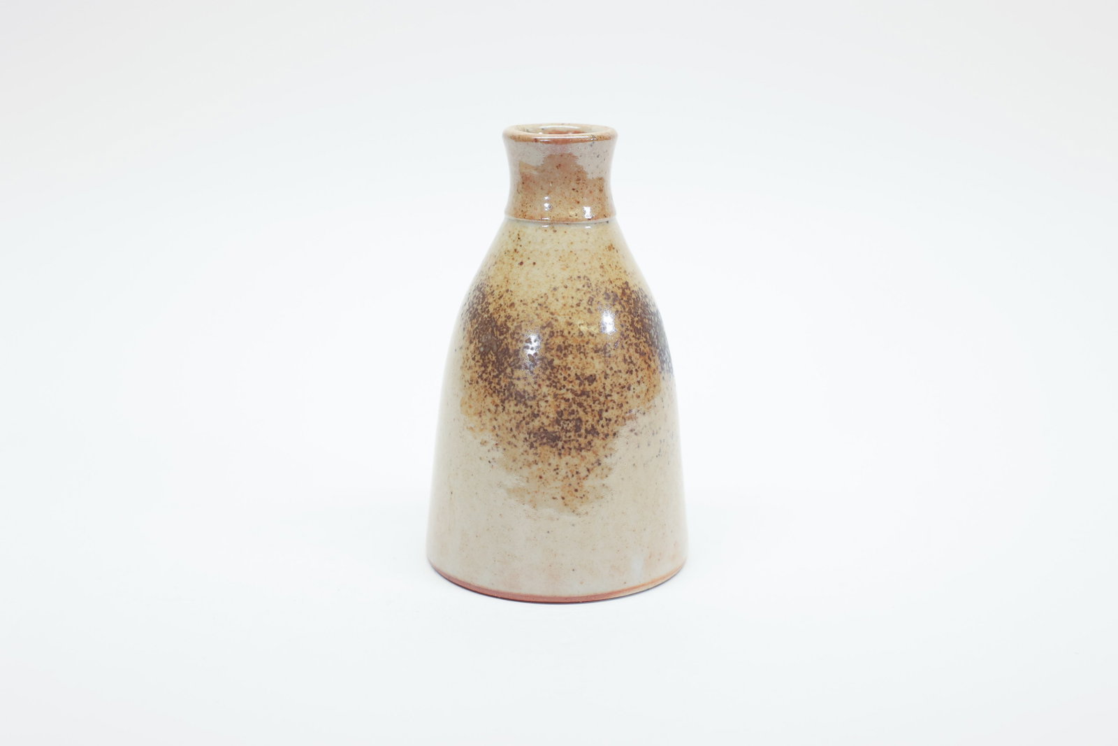 Whitefish Pottery Bud Vase, Montana, 2013: Description:Hand-thrown stoneware bud vase with a tapered conical body and short flared neck, finished in a speckled cream and tan glaze with mottled brown patches and a soft rose-pink blush near the