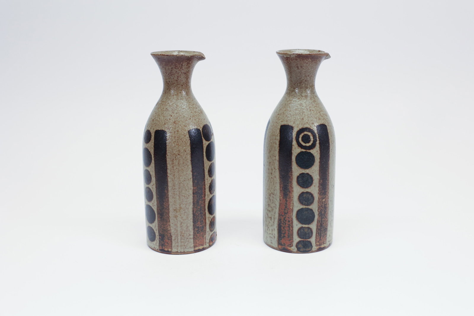 OMC Stoneware Oil and Vinegar Cruets, Pair: Description:Pair of hand-thrown stoneware cruets/bottles with a speckled tan-gray glazed body, a brown rim and pouring spout, and bold hand-painted geometric decoration in black — vertical stripe ba