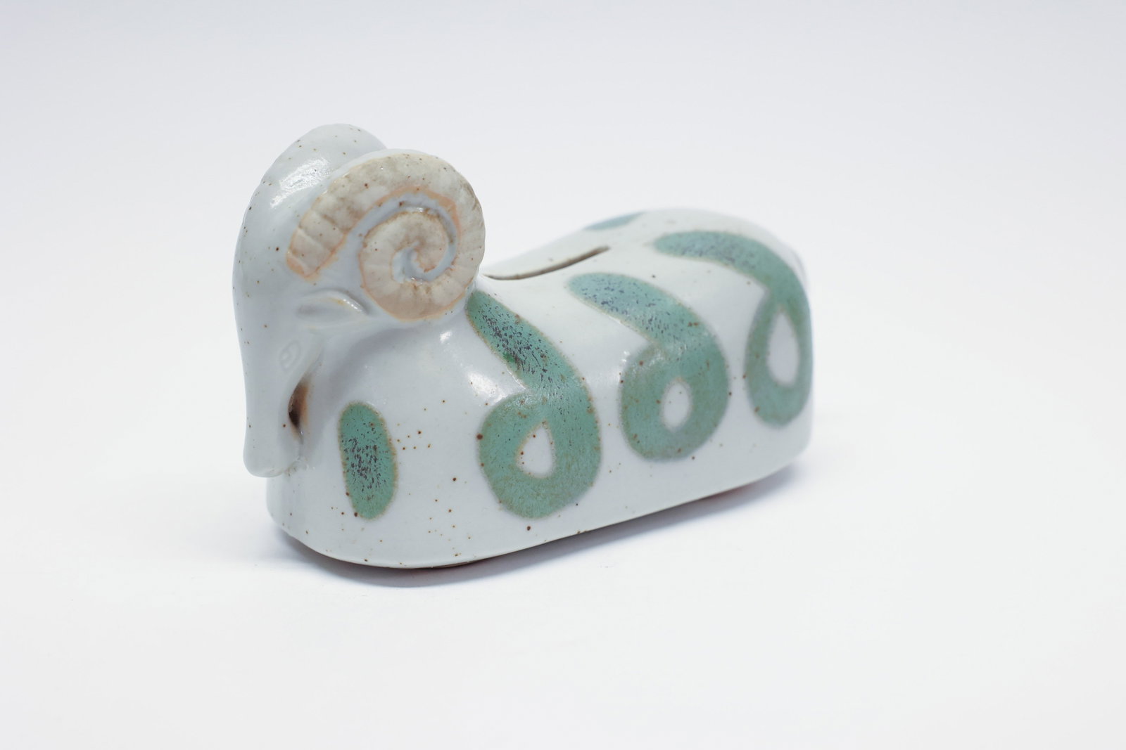 Takahashi Ceramic Ram Figural Coin Bank: Description:Whimsical ceramic figural coin bank in the form of a ram, with a glossy white glazed body decorated with hand-painted sage-green scroll/wave motifs, and large curled horns detailed in tan 