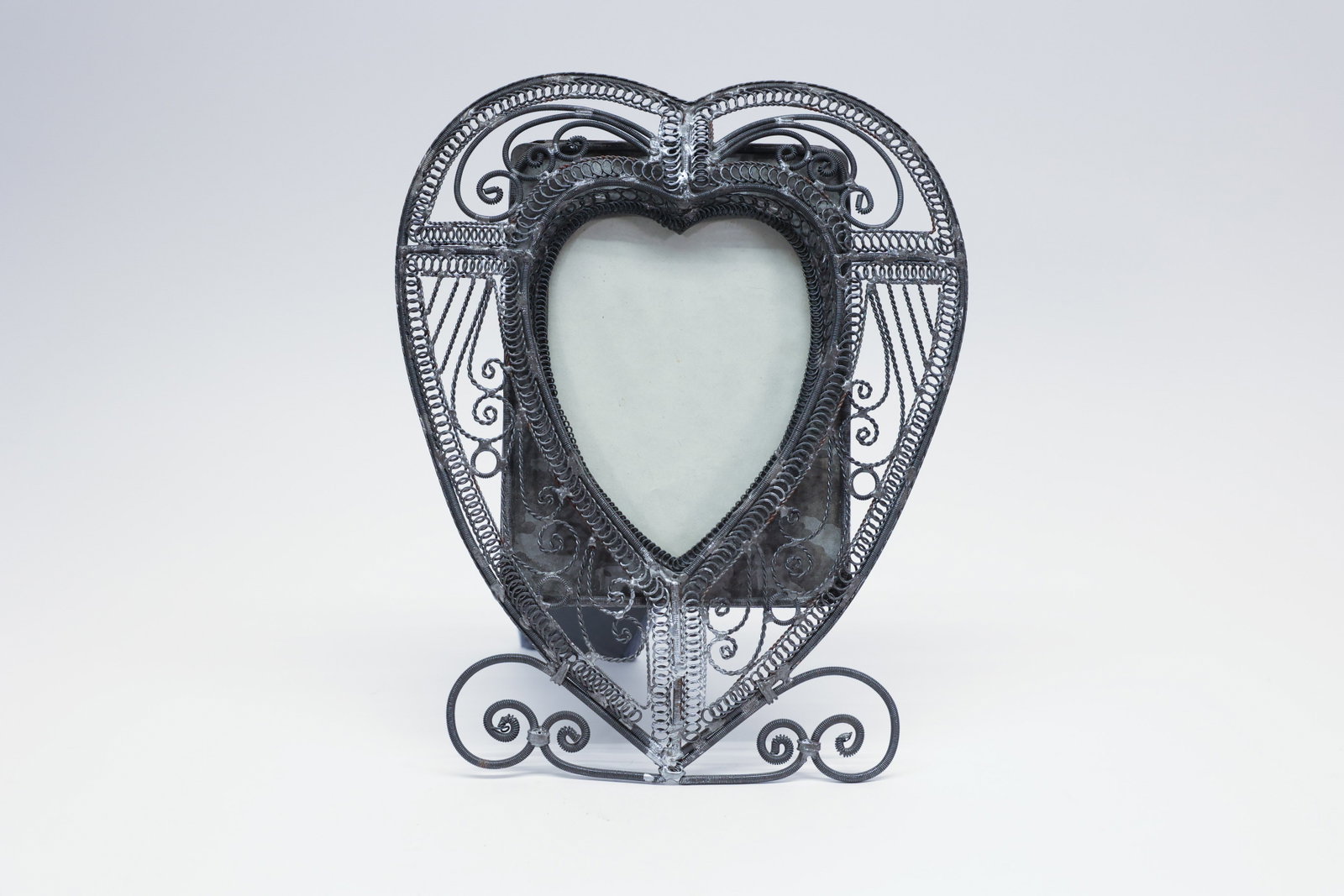 Vintage Mexican Filigree Wire Heart Photo Frame: Description:Vintage heart-shaped photo frame made of intricately coiled and scrolled wirework, with a dense filigree pattern of ropetwist coils, scrolls, and openwork panels surrounding a heart-form