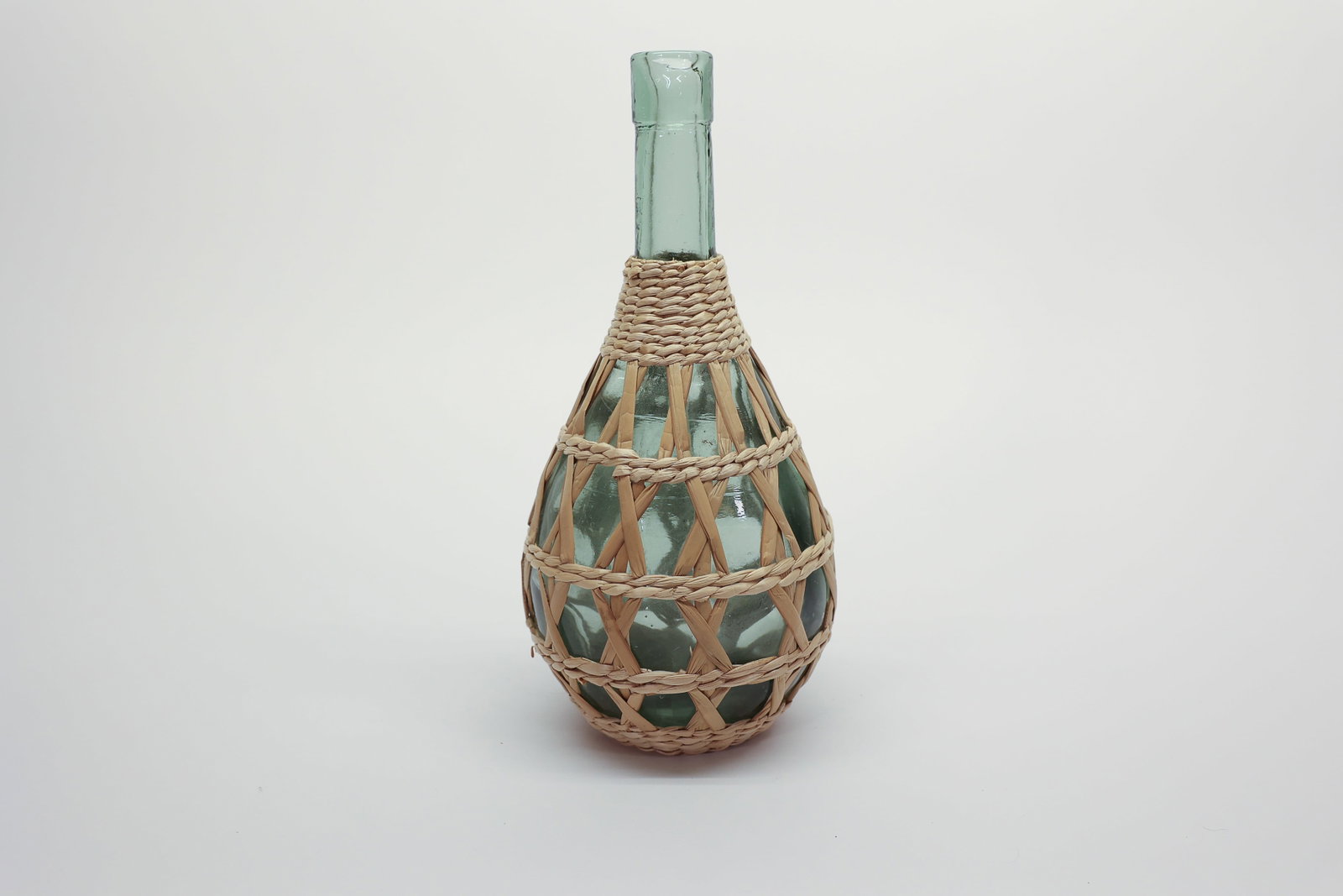 Wicker-Wrapped Demijohn Bottle Coastal Decor: Vintage glass demijohn bottle, beautifully encased in its original, hand-woven wicker basket. This timeless piece perfectly bridges the gap between old-world European charm and airy, modern design. It