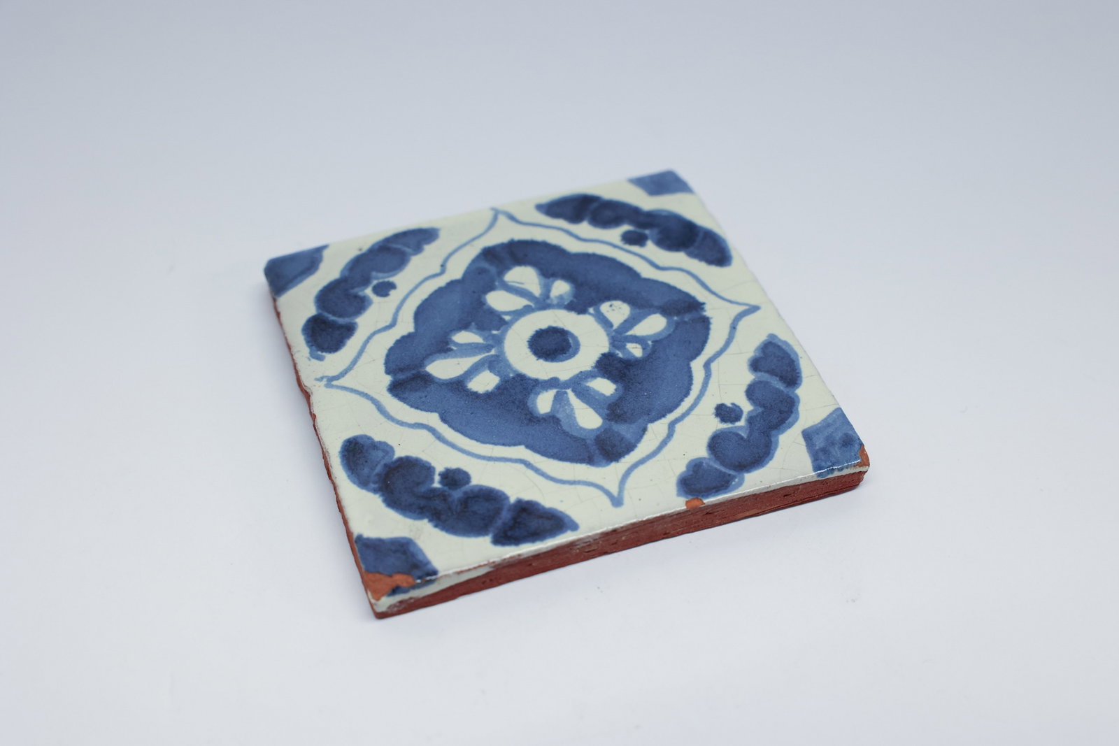 Blue & White Hand-Painted Talavera-Style Tile: Description:A single hand-painted terracotta tile decorated in cobalt blue on a white tin-glazed ground, with a central floral medallion framed by a scalloped border and cloud-like corner motifs. The 
