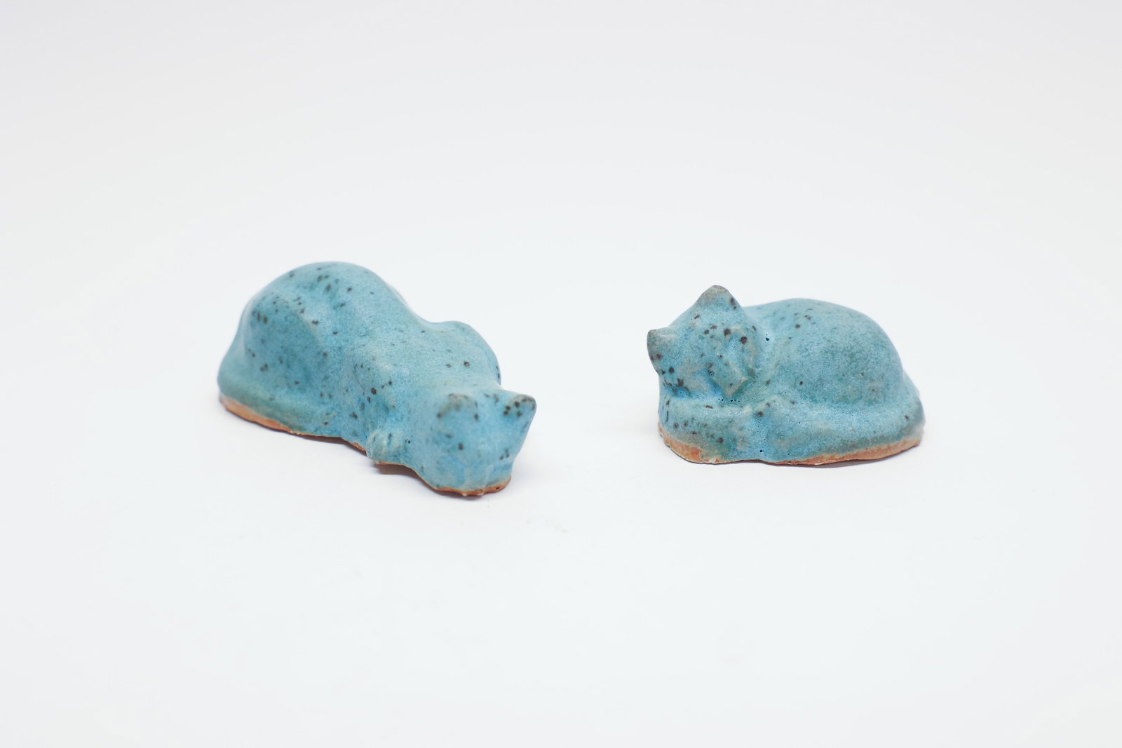 Pair of Turquoise Blue Glazed Pottery Cats: Description:A pair of small studio pottery cat figurines, each depicting a curled, sleeping cat with its tail wrapped around its body. Both are glazed in a mottled turquoise blue with scattered dark s