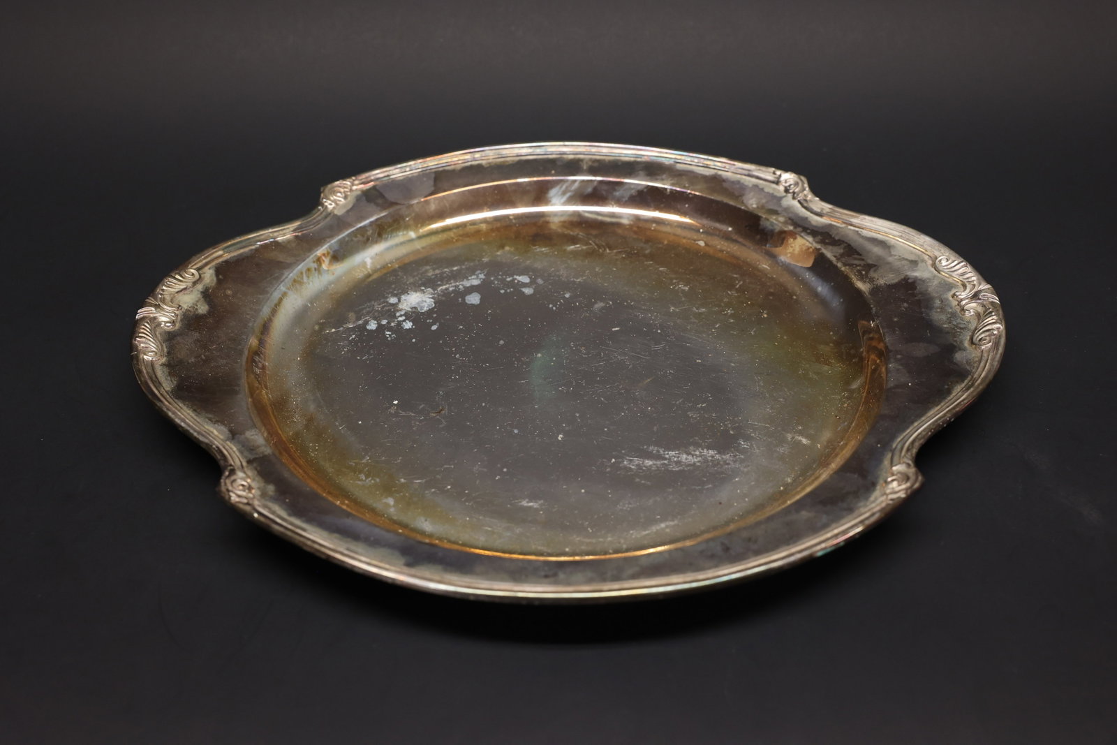 Scrolled-Edge EPNS Silver-Plate Serving Tray: Round serving tray in silver plate with a scalloped rim and scroll-and-shell edge detail, twin integrated handles. Marked "EPNS" with a pattern number and a small maker's mark on the underside, though