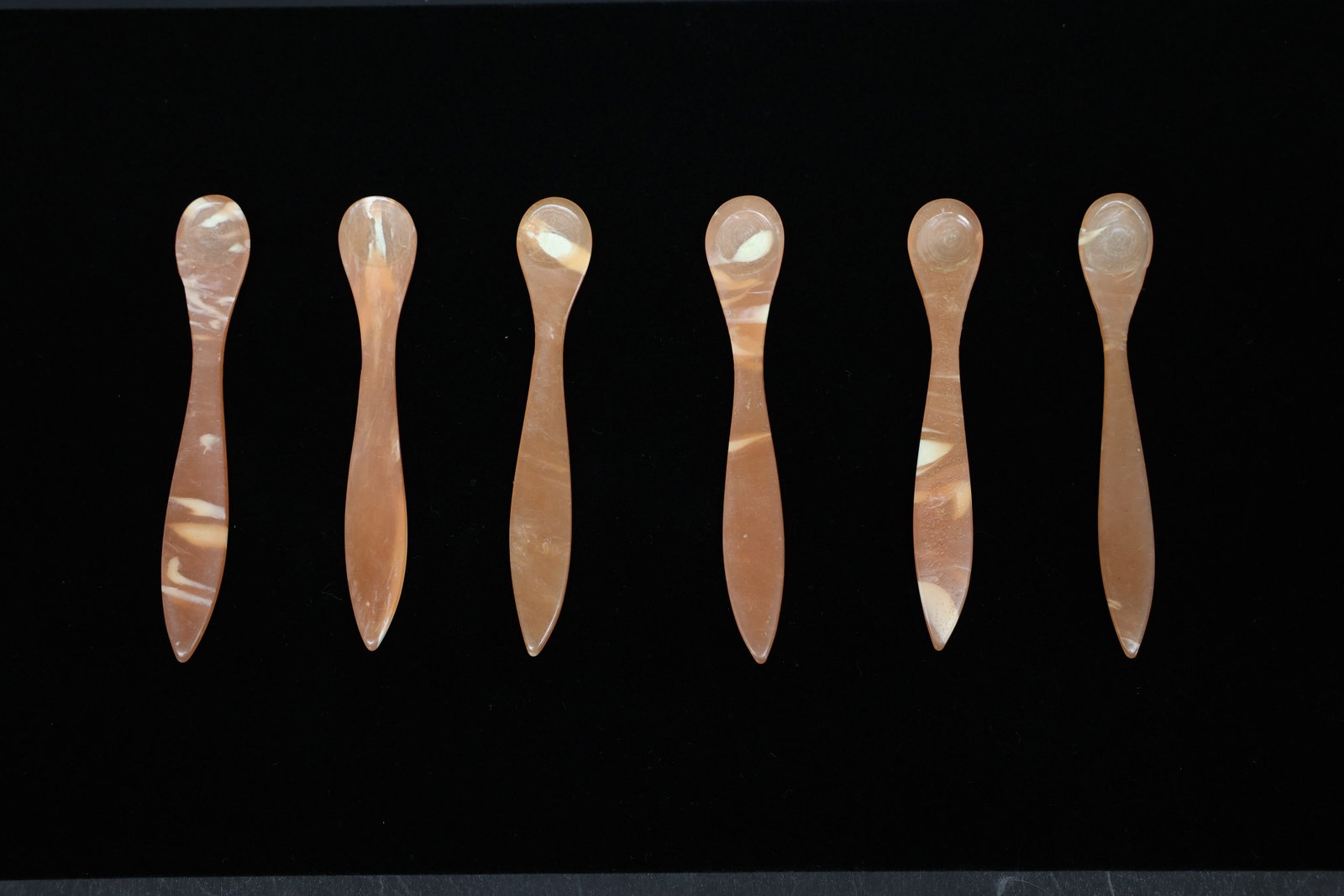 Set of Six Carved Salt or Caviar Spoons: Set of six small carved spoons, each with a rounded bowl and slender tapered handle. Translucent honey-tan material with natural mottled banding characteristic of horn. Horn spoons were traditionally 